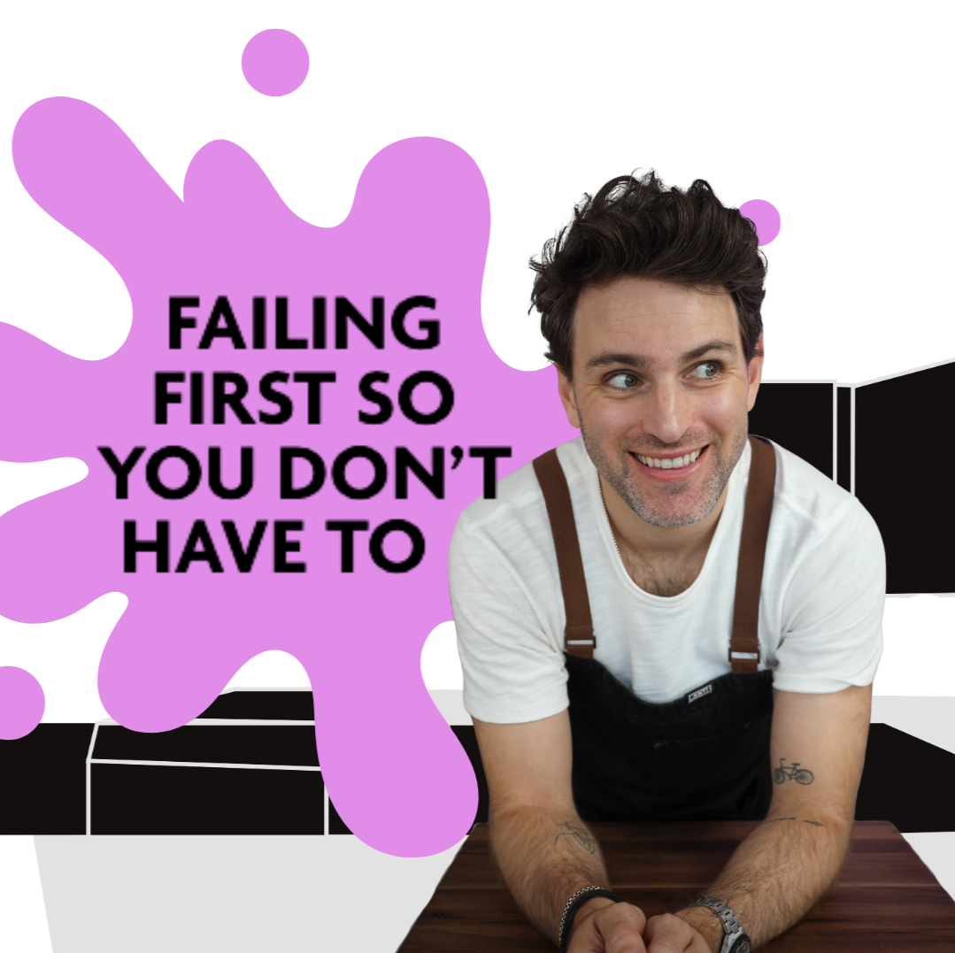 A man with dark, curly hair and a beard, smiling, wearing a white t-shirt and black overalls, leaning on a wooden table. Behind him is a purple background with a speech bubble that says, 'Failing first so you don't have to'.