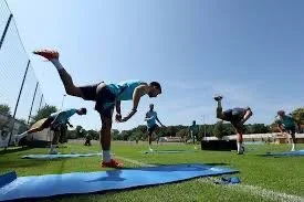 People practicing yoga outdoors on a sunny day, balancing on one leg on blue yoga mats.