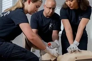 Three people practicing CPR on a mannequin during a training session.