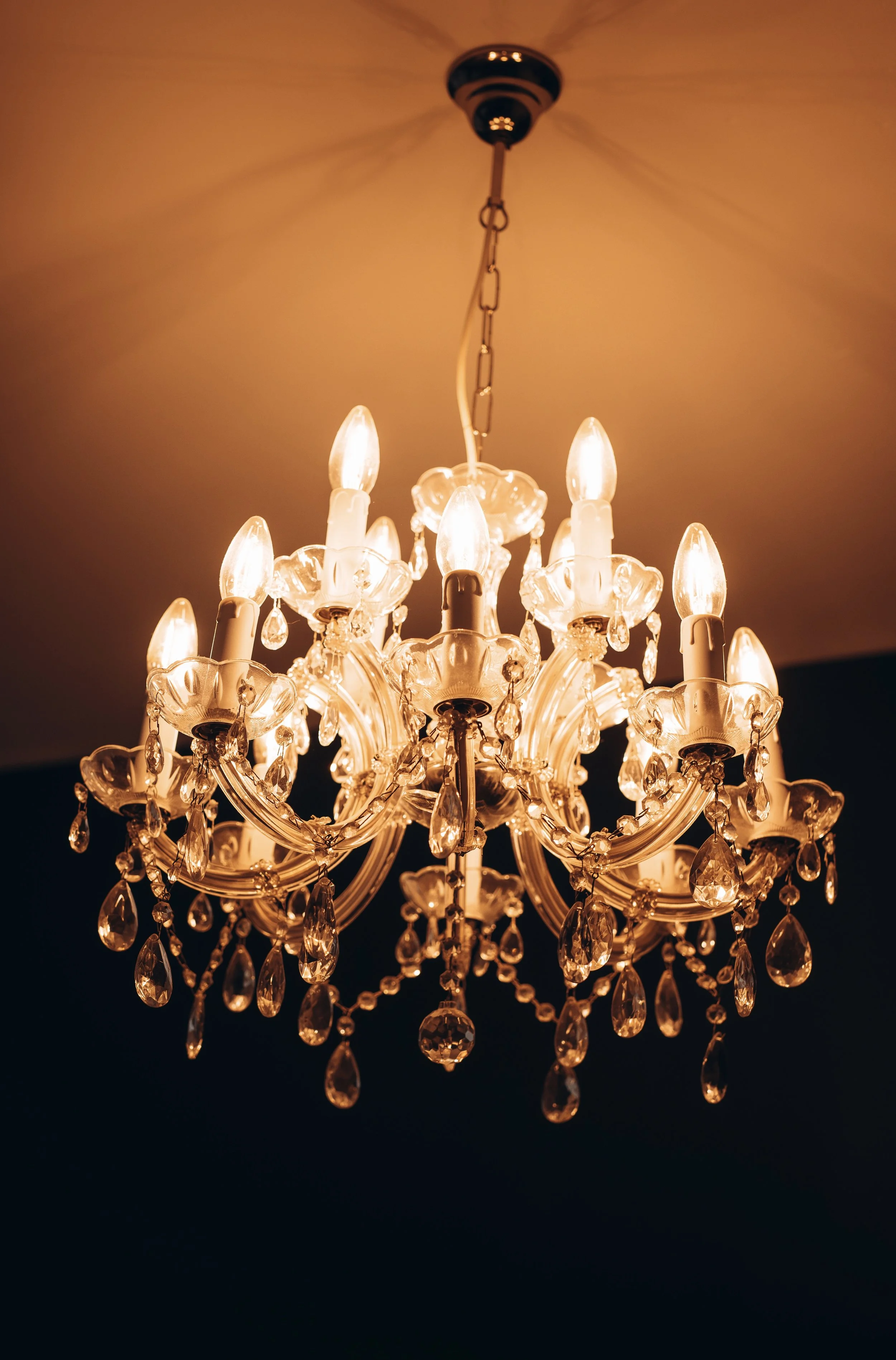 Elegant crystal chandelier hanging from the ceiling, lit with multiple bulbs, creating a warm glow.