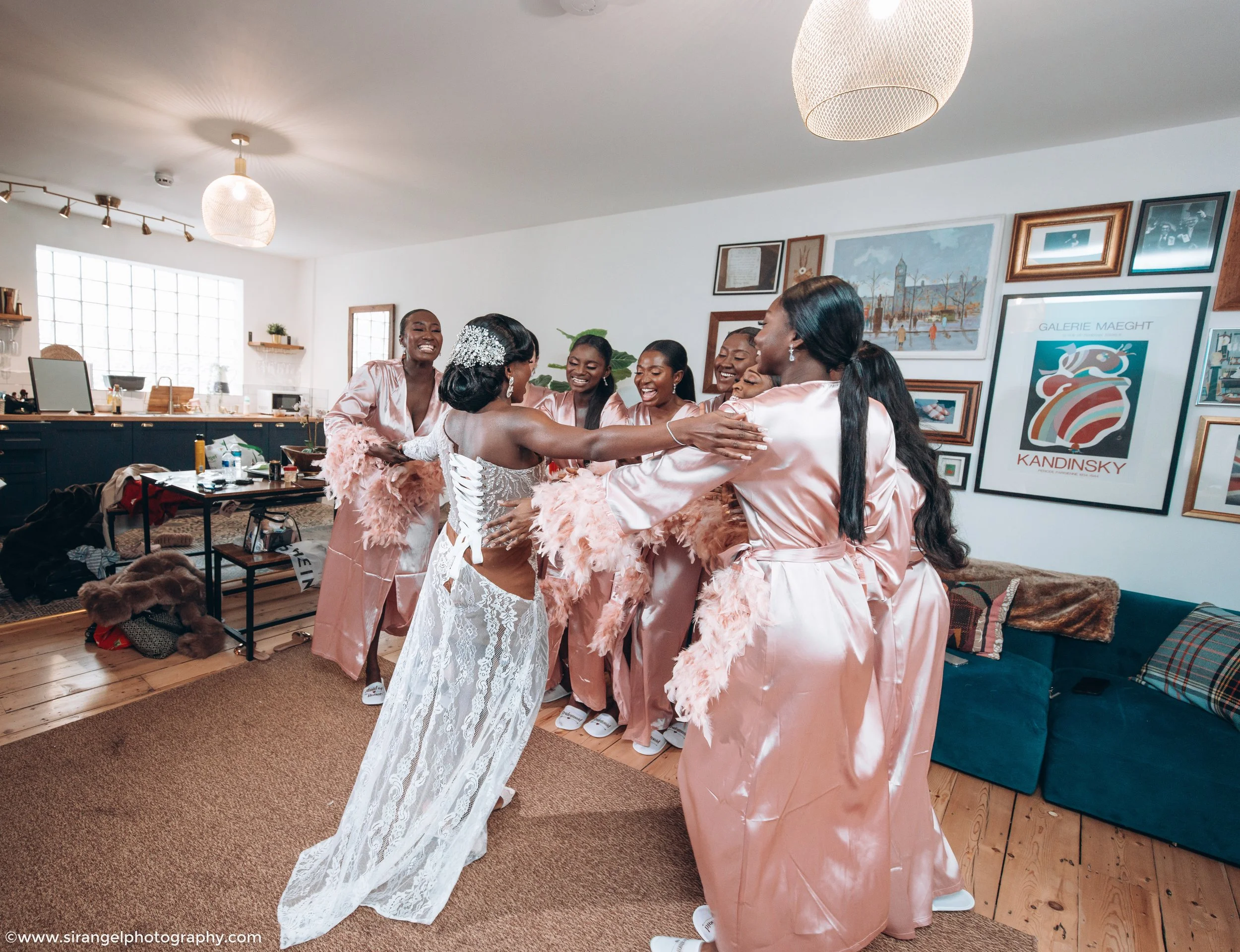 Bride hugging bridesmaids in robe in a cozy room with art on the wall