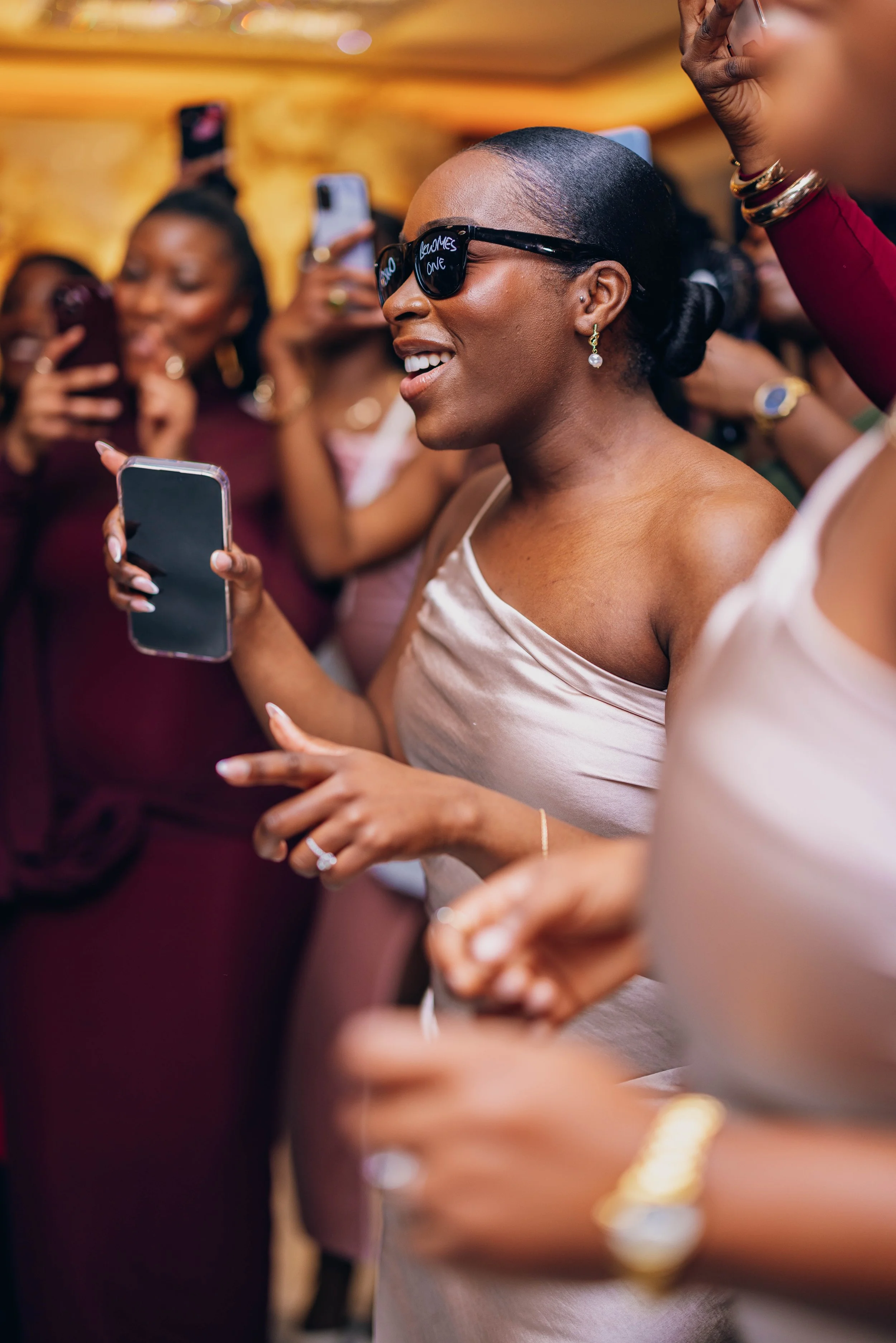Women at a party taking and enjoying photos with their smartphones, some wearing sunglasses and dresses.