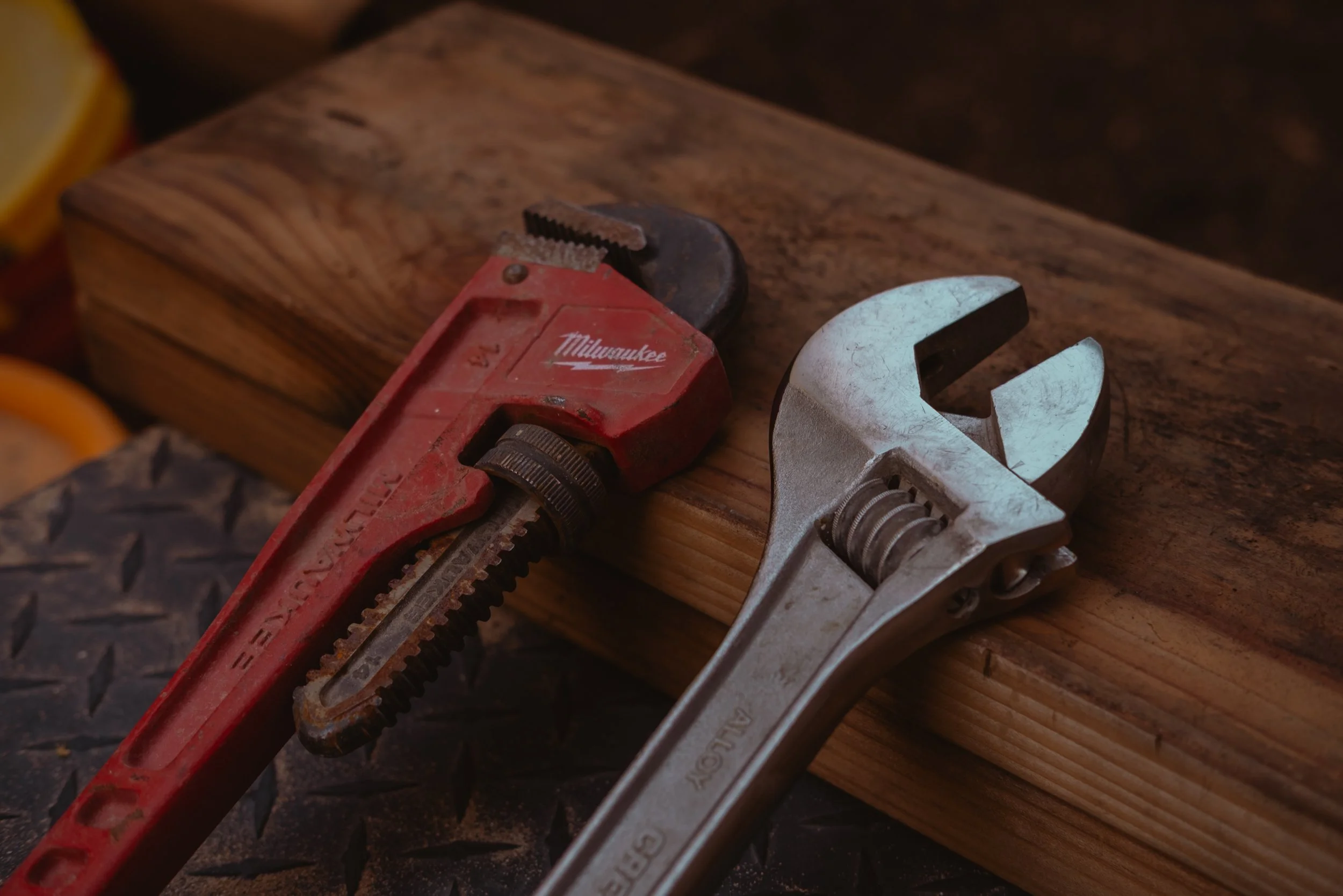 A red Milwaukee pipe wrench and a silver adjustable wrench resting on a wooden surface, as used by Holda Handyman, a trust handyman servicing Gilbert, Arizona and the East Valley.