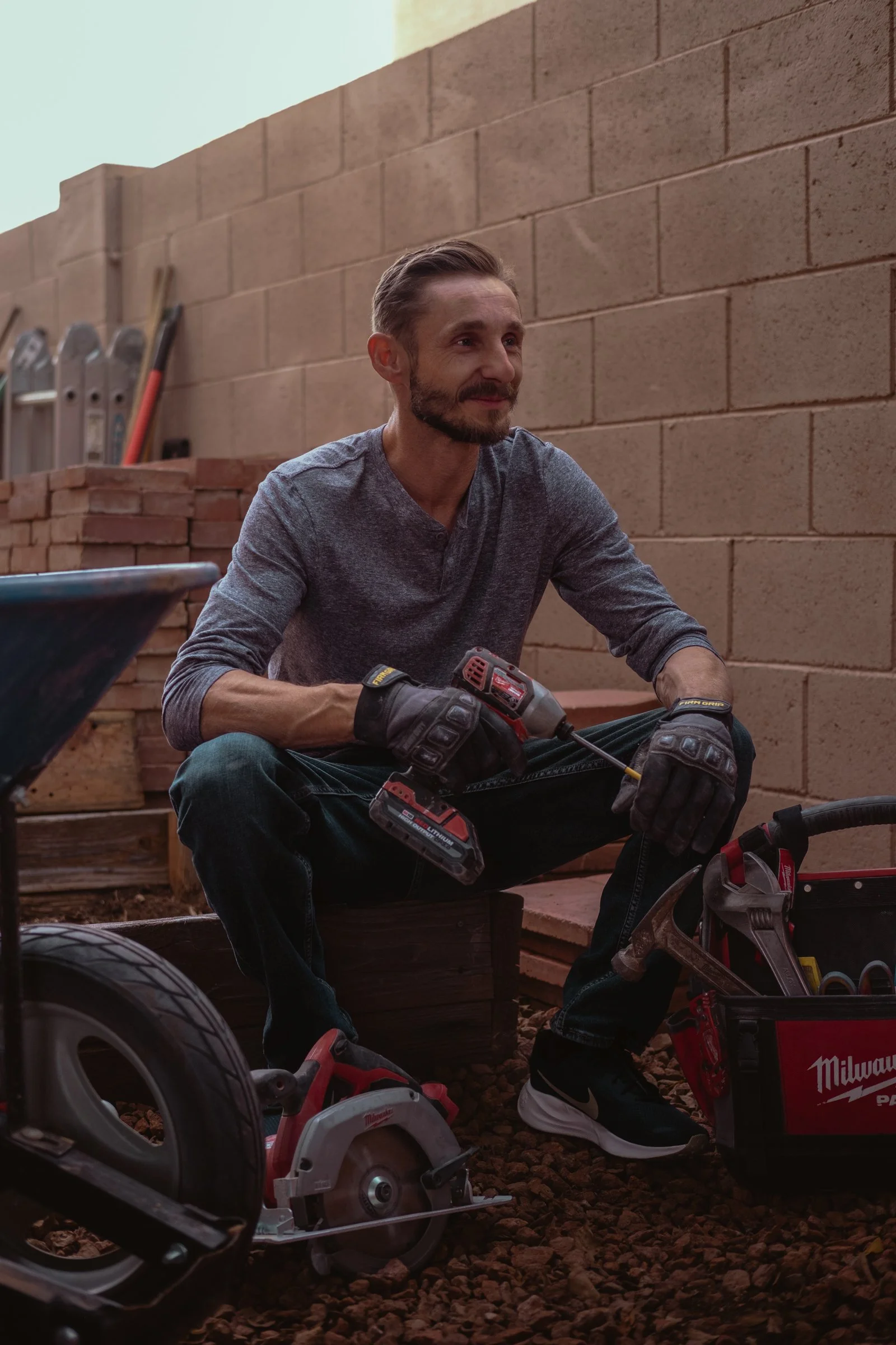 Mariusz Holda, owner of Holda Handyman, sitting atop a stack of bricks with various power tools around him in the midst of a handyman home renovation project in Gilbert, Arizona.
