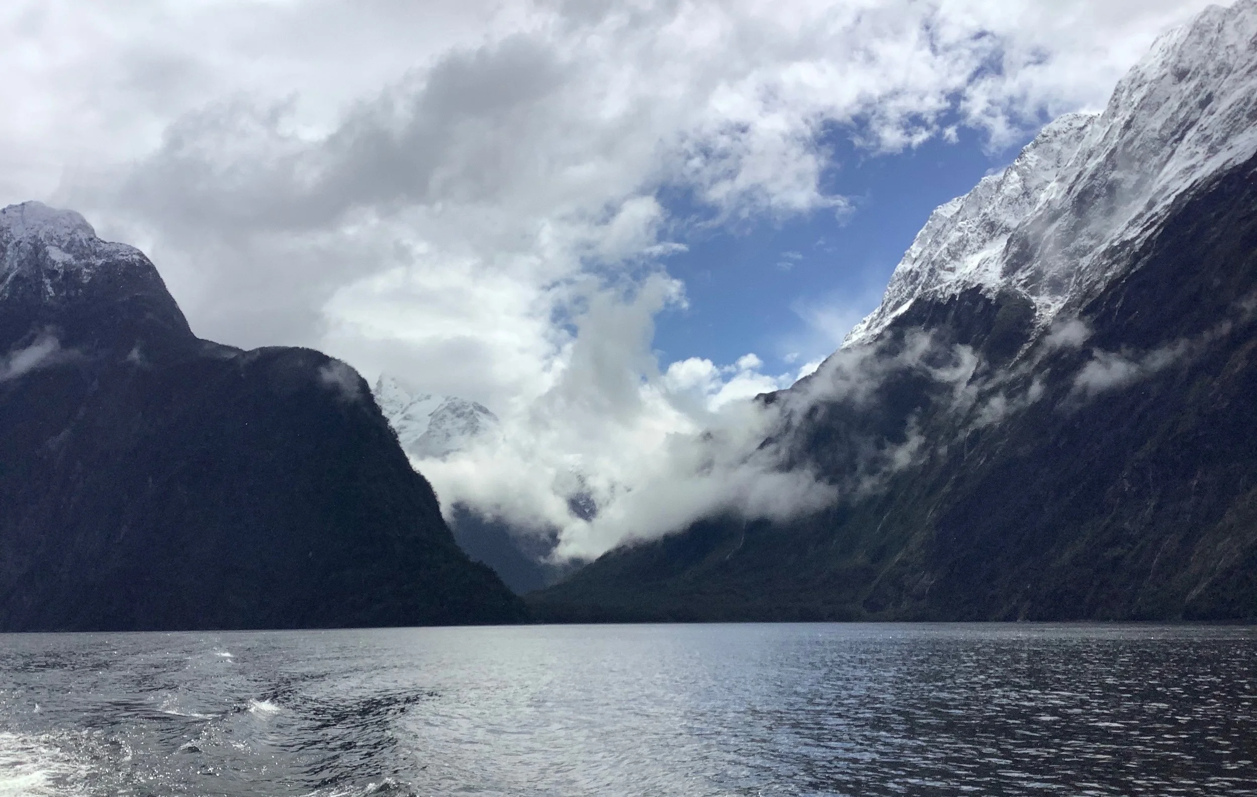 Snow-capped mountains surrounding a body of water with clouds in the sky.