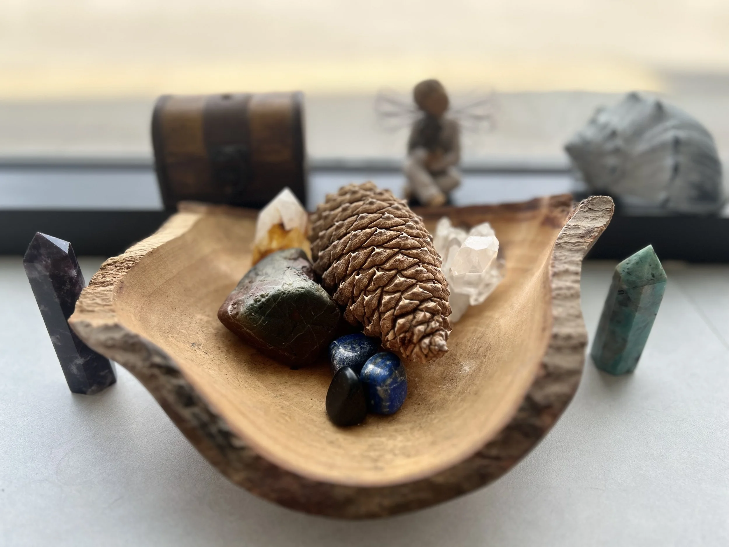 Wooden bowl containing a pine cone, various crystals, and a small figurine with wings.