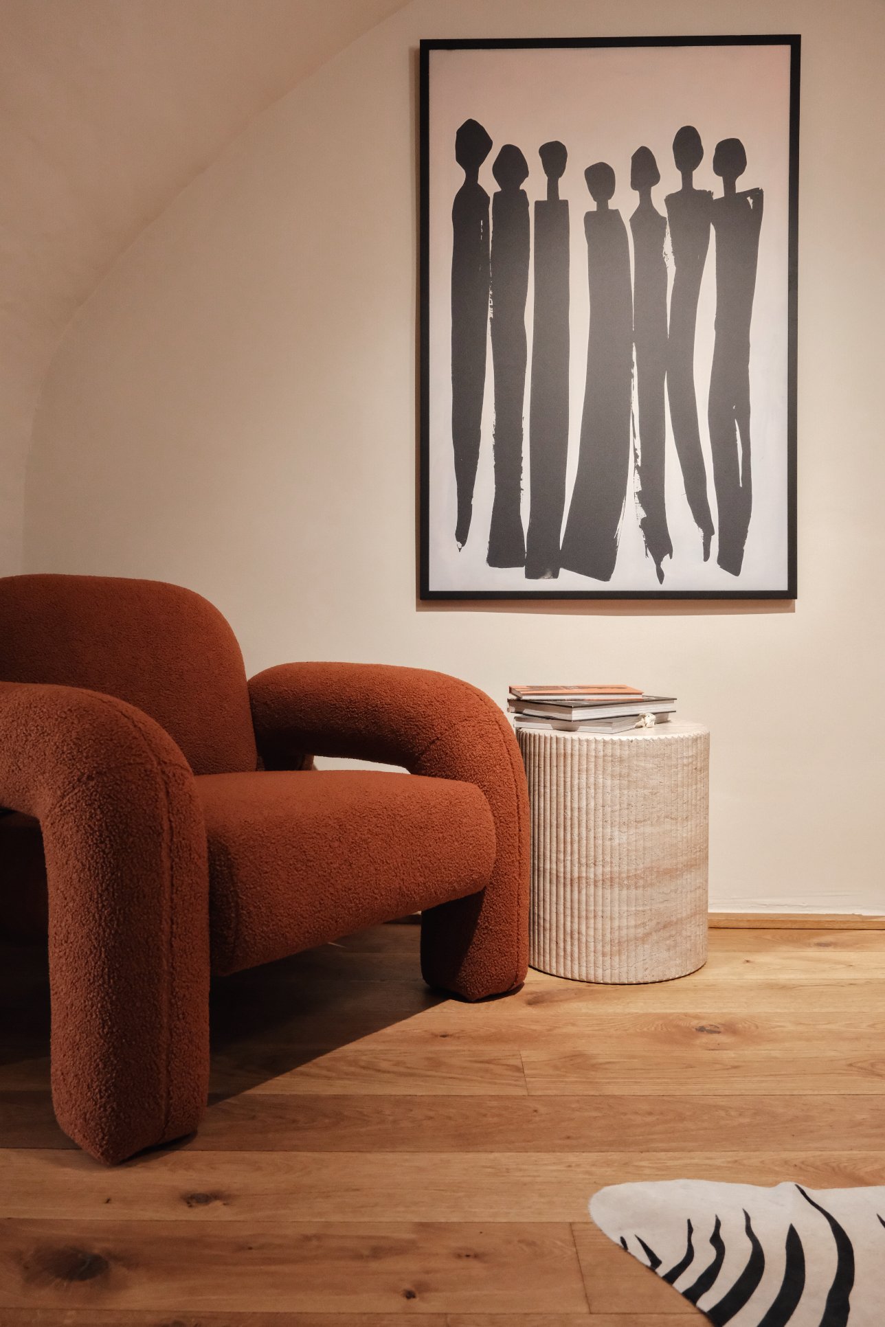 Ein Wohnzimmer mit einem braunen, weichen Sessel, einem runden Beistelltisch aus hellem Holz, einer schwarzen und weißen Wandkunst, einem Stapel Zeitschriften auf dem Tisch und einem Zebra-Teppich auf Holzboden.