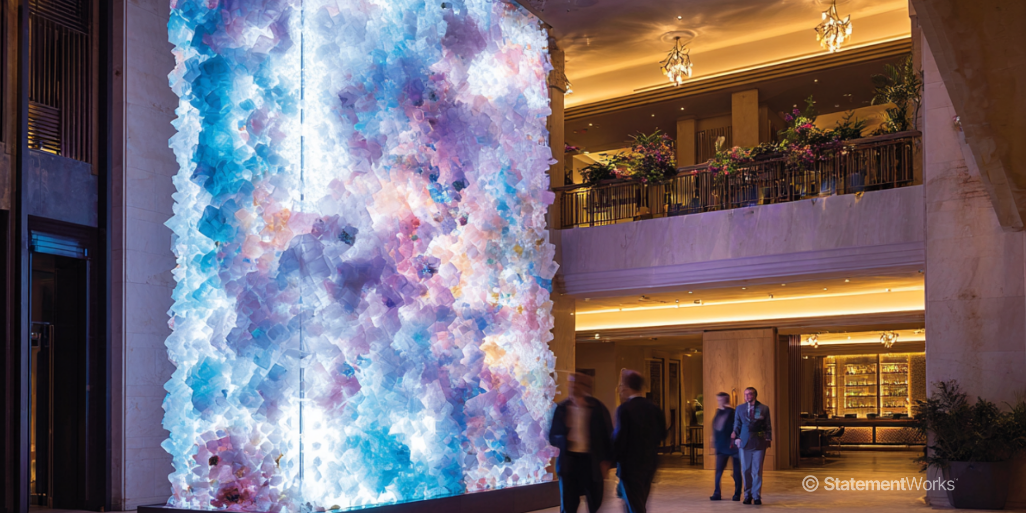 An indoor sensory illuminated tower in a luxurious hotel lobby or shopping mall with marble walls, a large colourful digital statement piece.