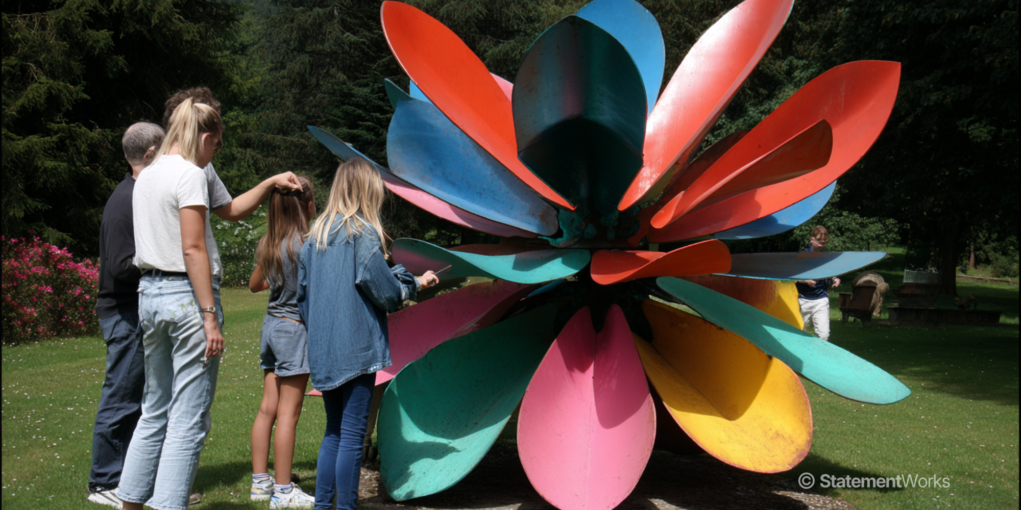 Family standing around a large kinetic flower shaped sculpture with coloured petals