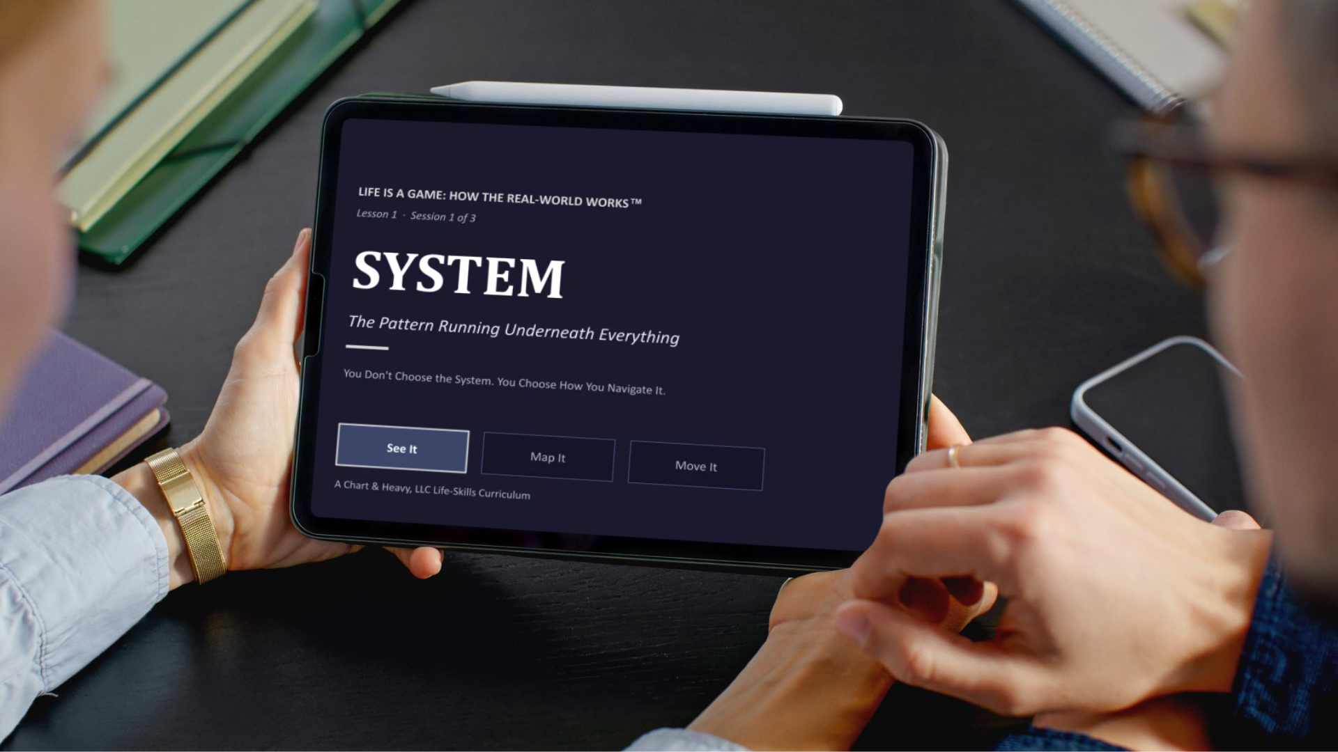 Person holding a tablet displaying a screen titled "System: The Pattern Running Underneath Everything" in a black and white design. The screen offers options labeled "See It," "Map It," and "Move It."