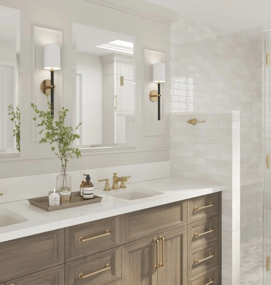 Bathroom with double vanity sink, gold fixtures, large mirror, white countertop, wall sconces, potted plant, bottles, and a glass shower enclosure with a white brick wall.