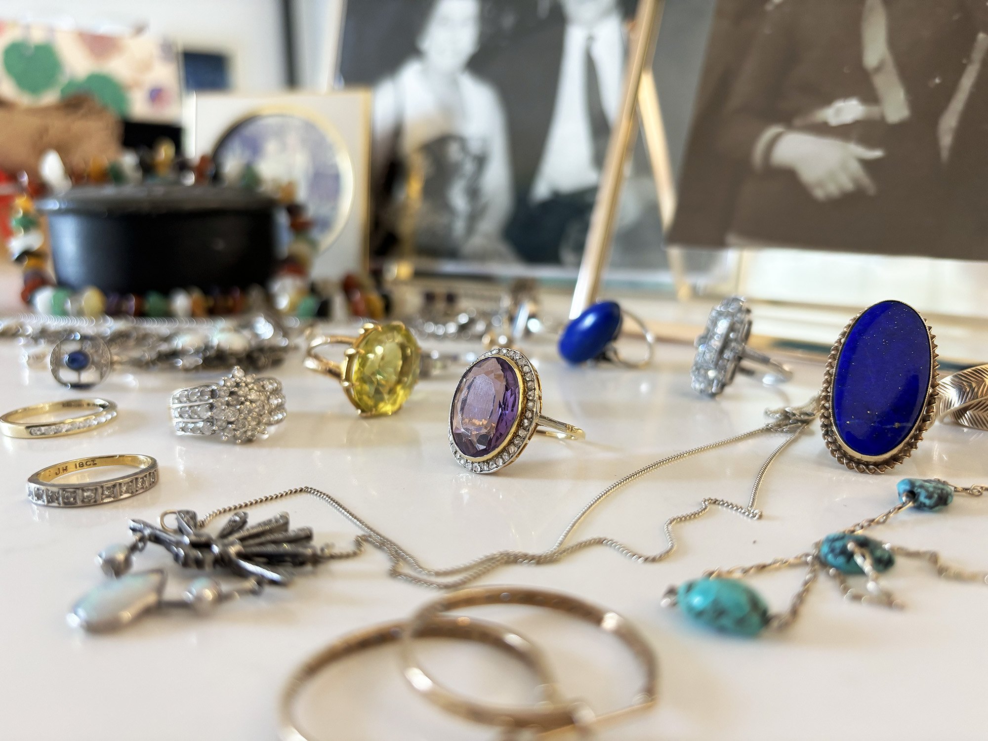A collection of jewelry including rings, necklaces, and bracelets displayed on a white surface, with a blurred background of an art area or studio.