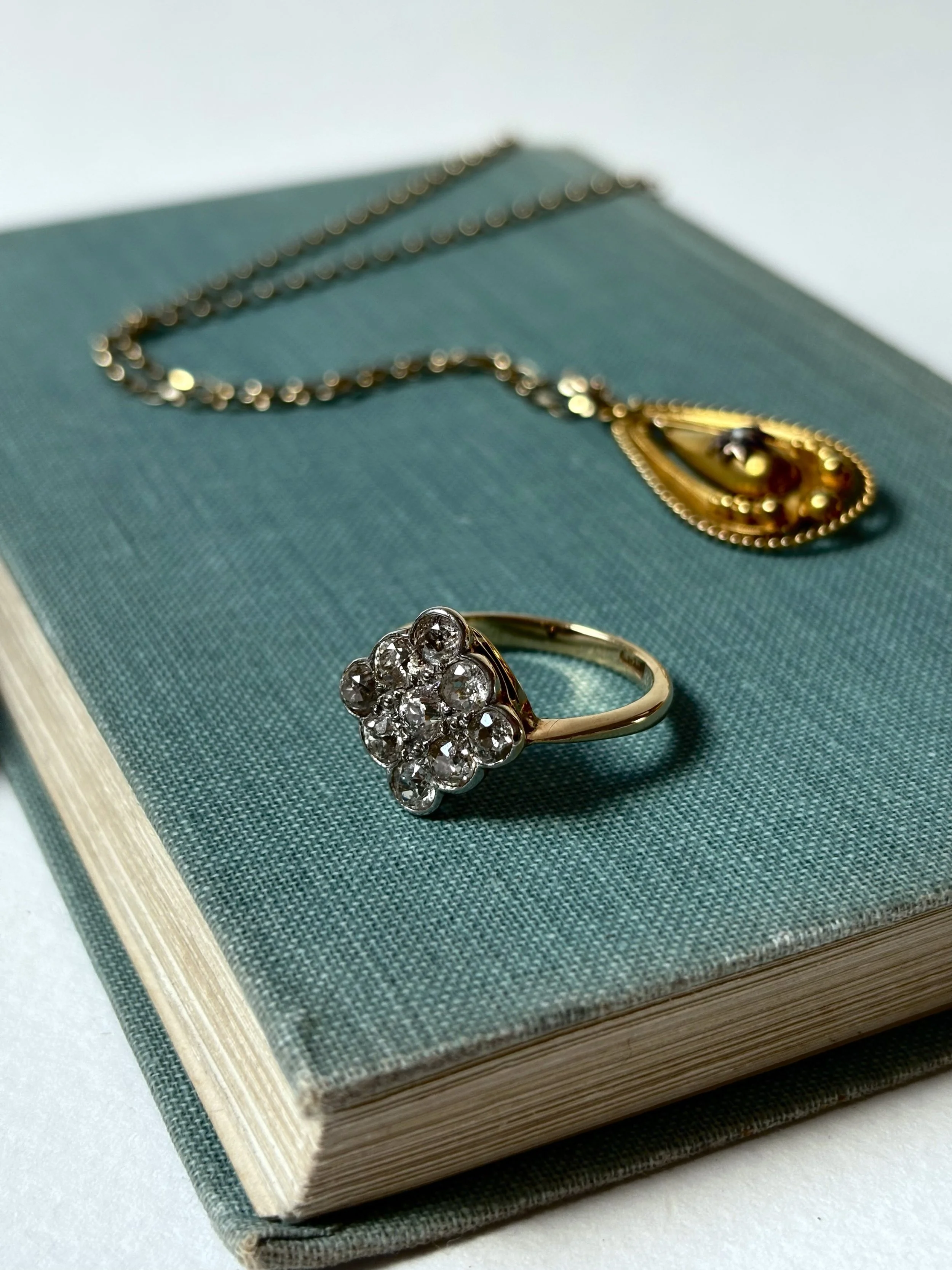 A diamond ring with a cluster of diamonds on a gold band, placed on a green-textured book.