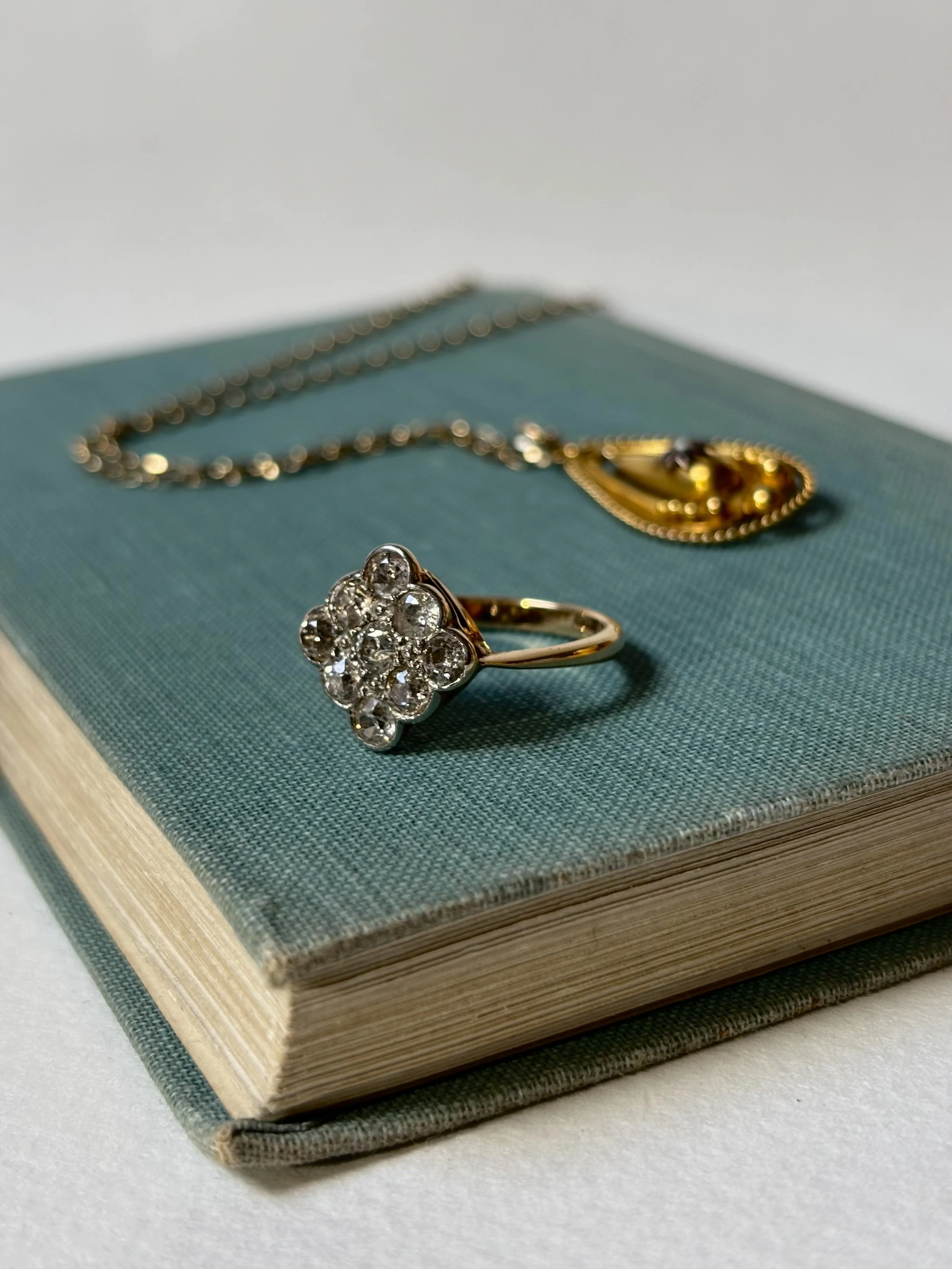 A gold ring with a cluster of diamonds placed on an old teal-colored book.