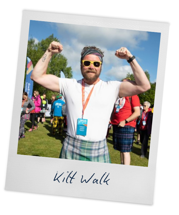 A man wearing a kilt flexes his muscles at the camera