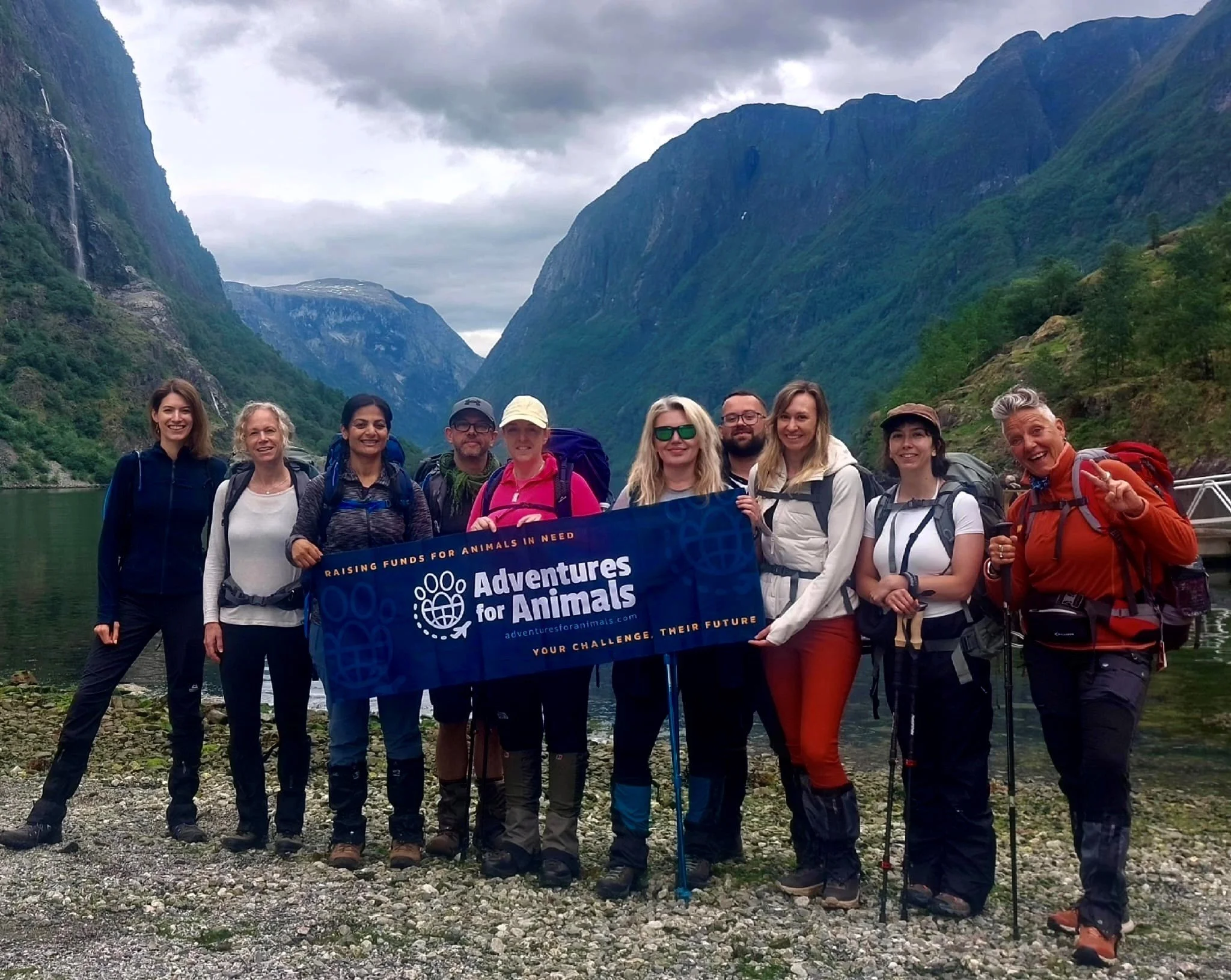 Group of hikers holding a blue "Adventures for Animals" banner in a scenic mountainous area