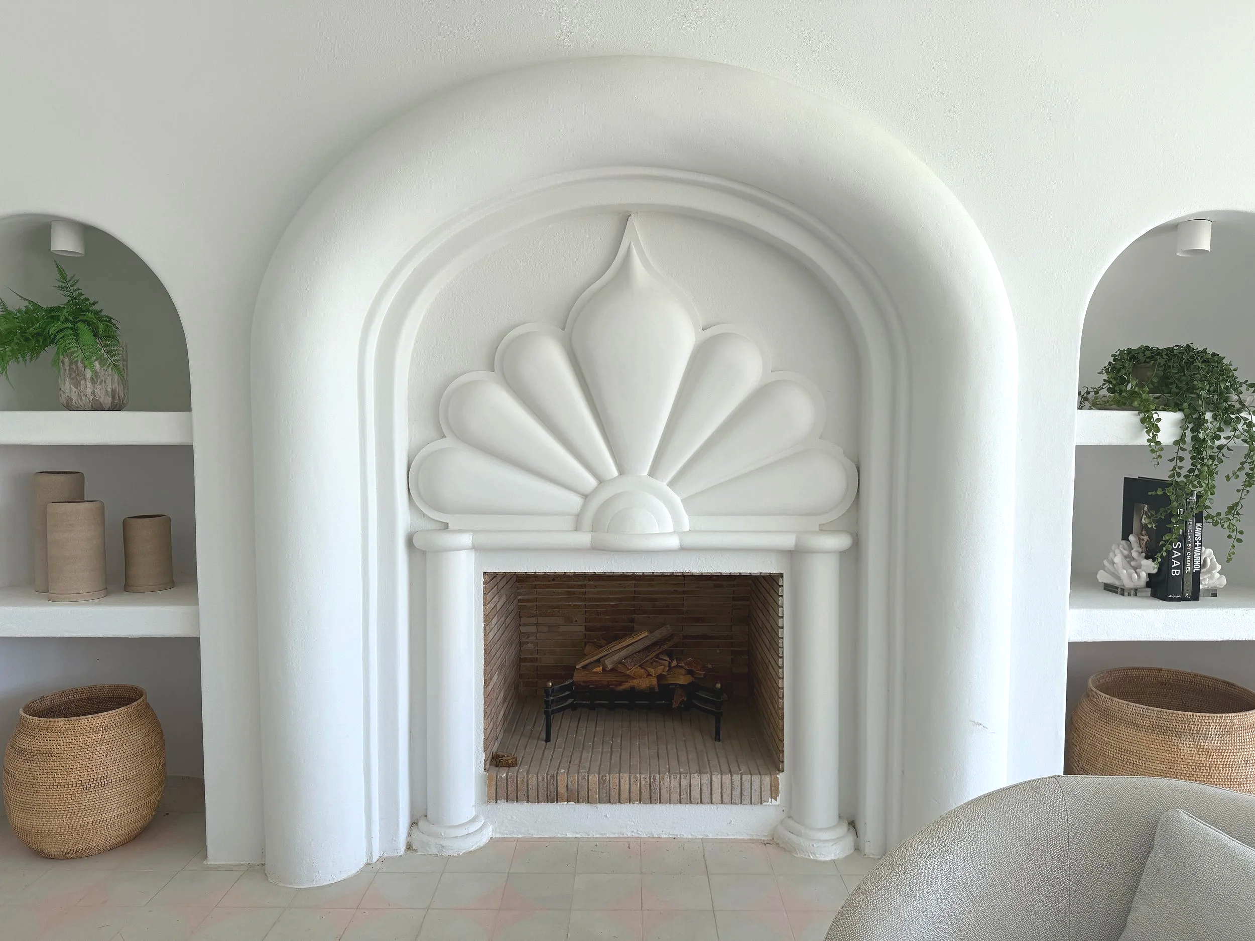 A white decorative fireplace with an artistic shell motif, flanked by built-in shelves with plants, books, and decorative objects.