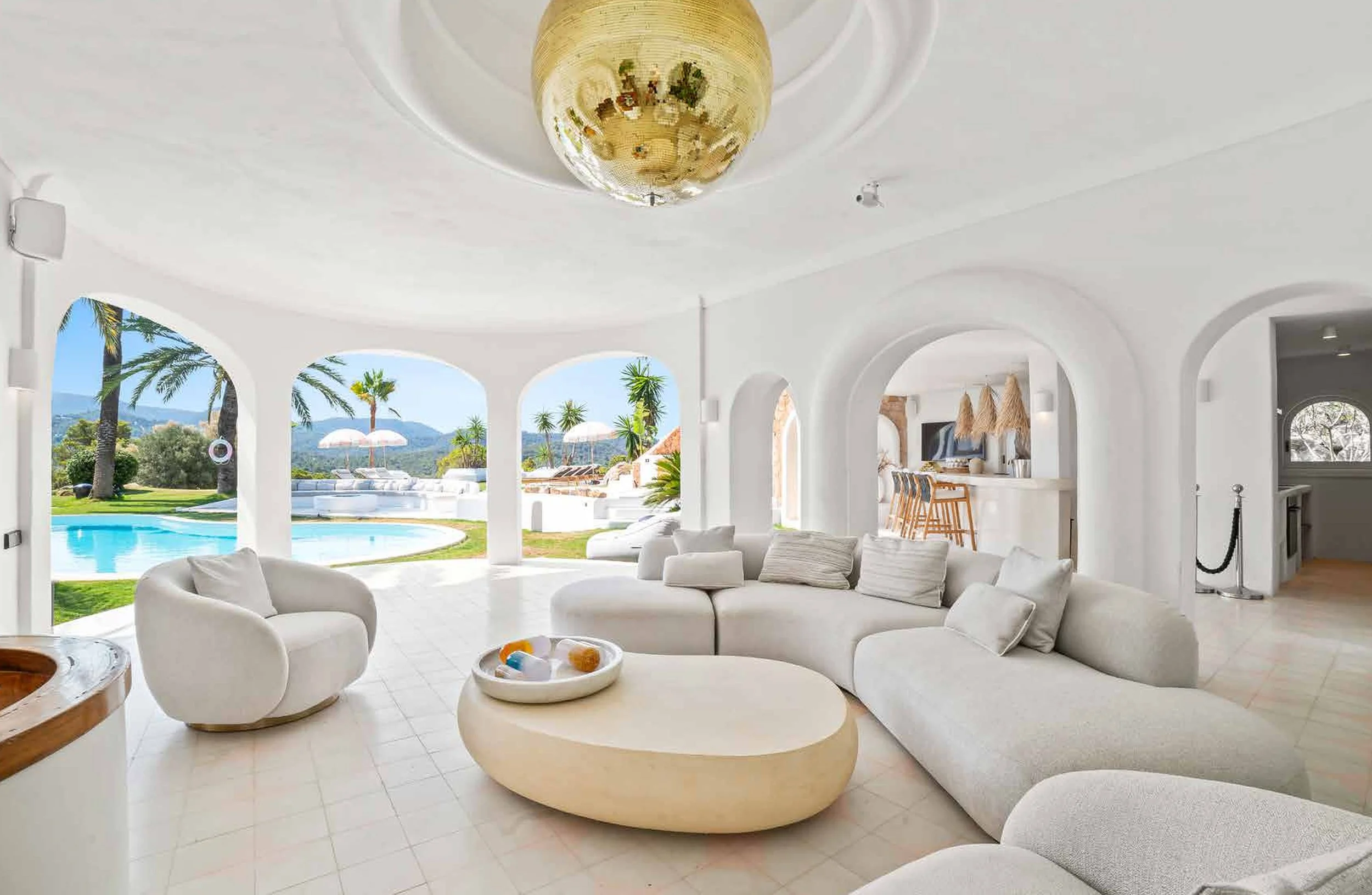 Living room with white furniture and large arches overlooking a pool and lush greenery outside.