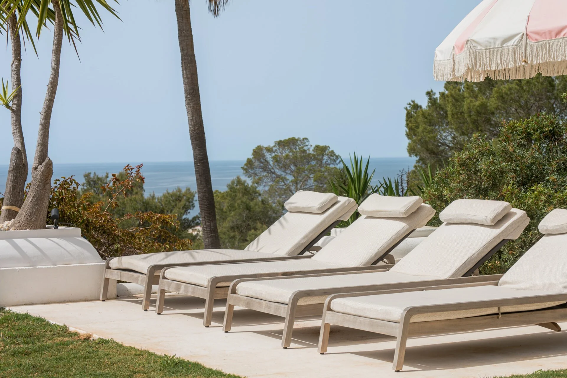 Beachside lounge chairs under an umbrella with palm trees and ibiza ocean in the background. Mediterranean film and shoot location in Ibiza.