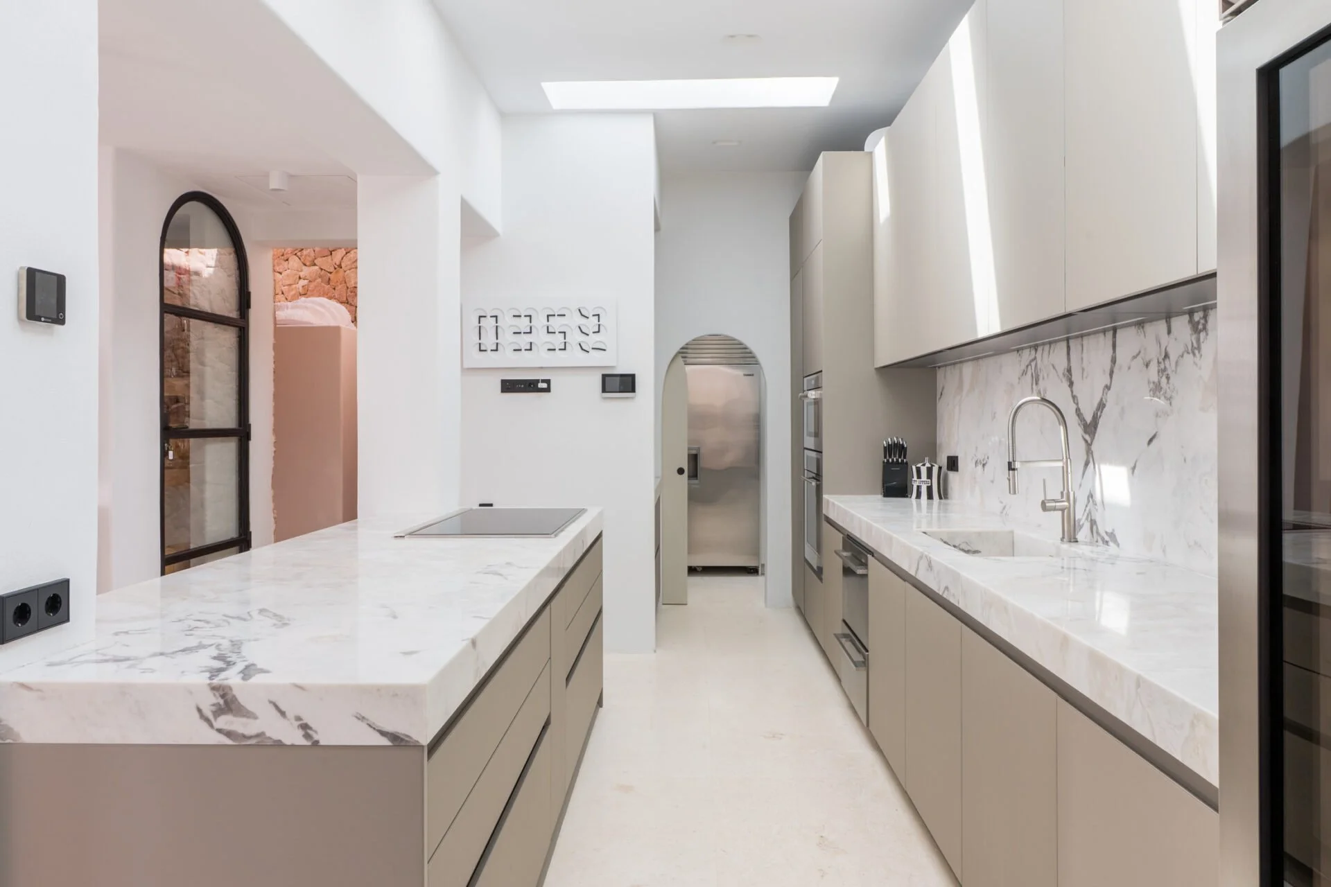 Modern kitchen with white marble countertops and beige cabinets, stainless steel appliances, and a skylight in the ceiling.