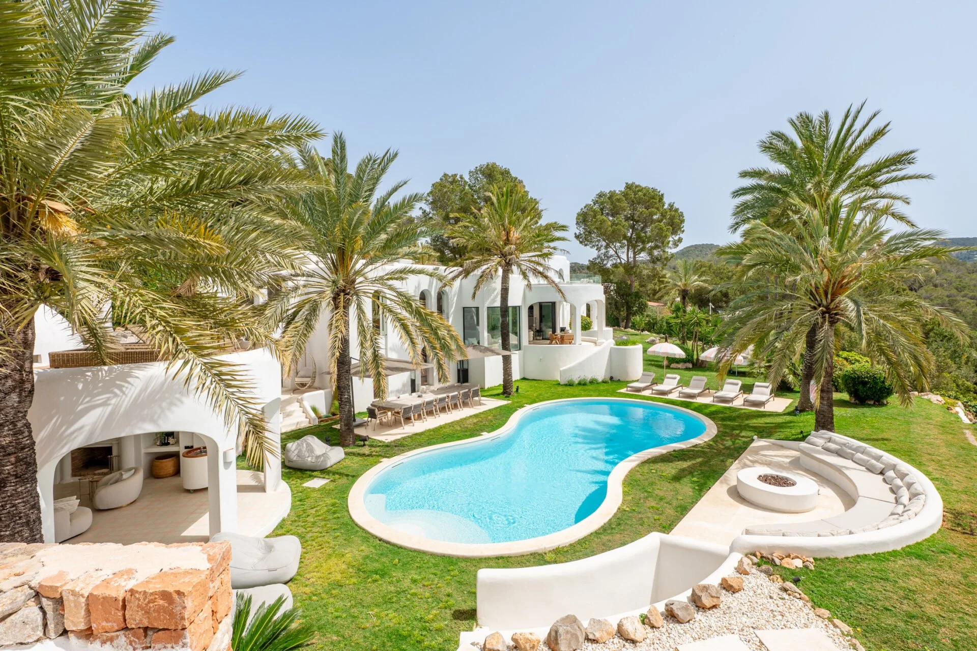 A luxurious outdoor pool area with white modern architecture and tall palm trees surrounding the pool on a clear sunny day.