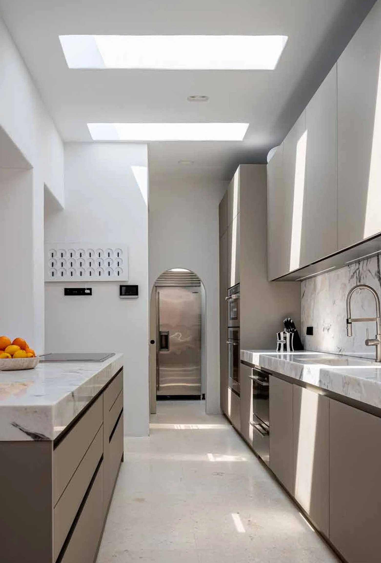 Modern kitchen with white and beige cabinets, marble countertops, built-in appliances, and skylights overhead.