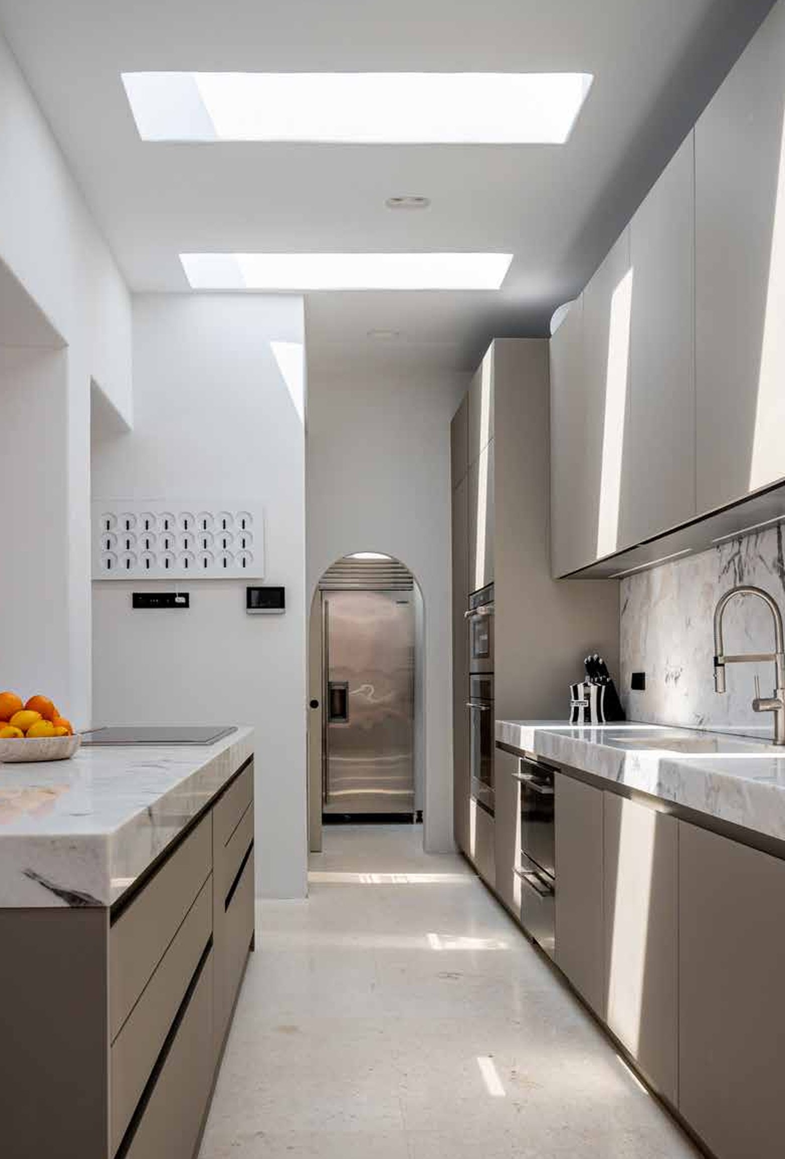 Modern kitchen with white cabinets, marble countertops, stainless steel appliances, and skylights letting in natural light.