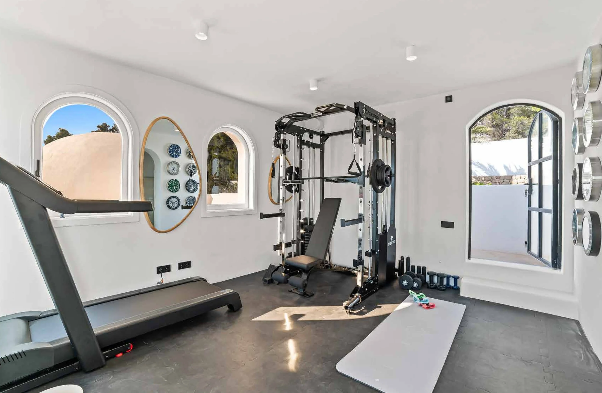 Home gym with treadmill, weightlifting equipment, and window views.