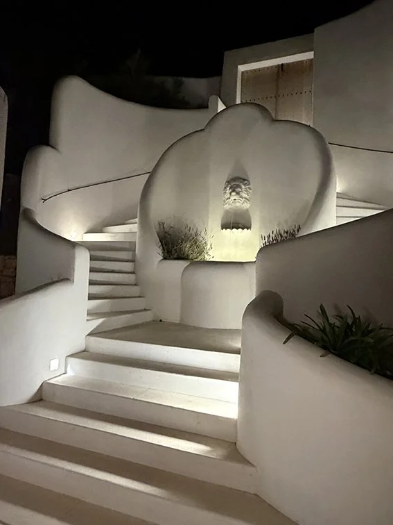 Night view of a modern, white, abstract architectural staircase with curved walls and an ornamental fountain feature at the top