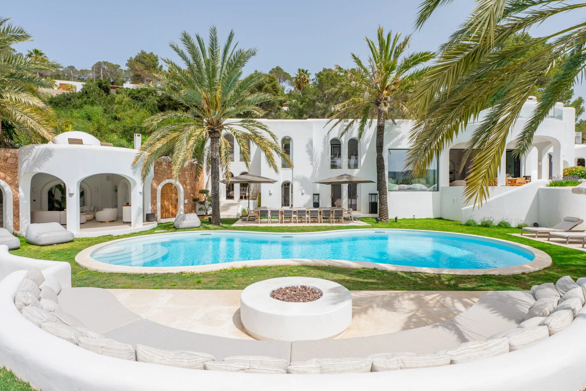Luxury white house with a swimming pool, surrounded by palm trees and outdoor furniture, in a lush green yard.