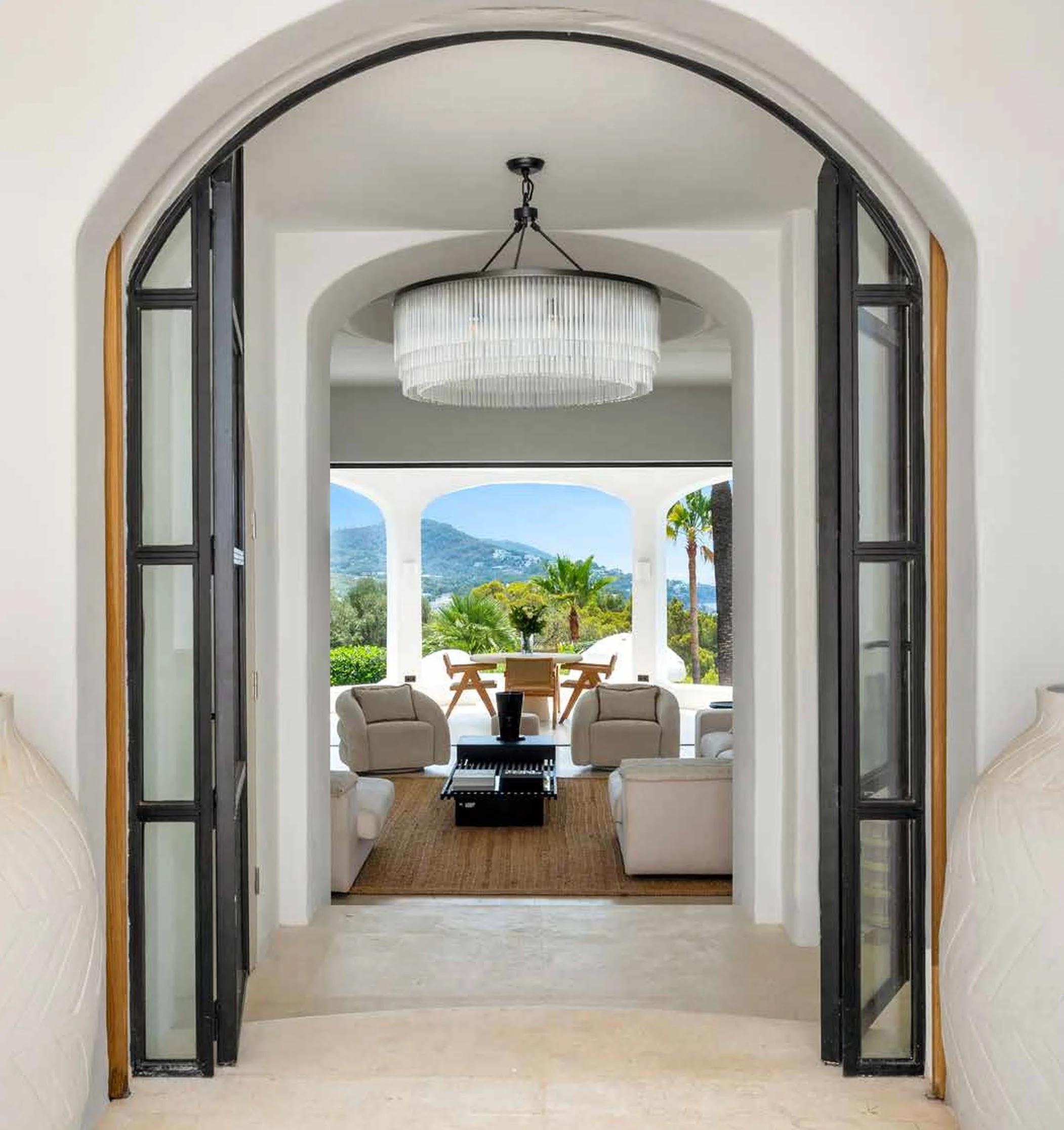 View through double glass doors into a sitting area with two armchairs and scenic outdoor landscape with mountains and palm trees.
