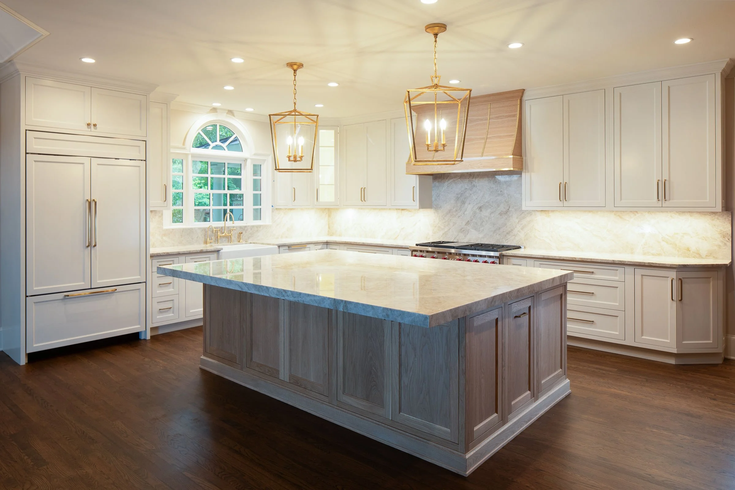 Bright kitchen with white cabinets, a large center island, wooden flooring, and modern lighting fixtures.