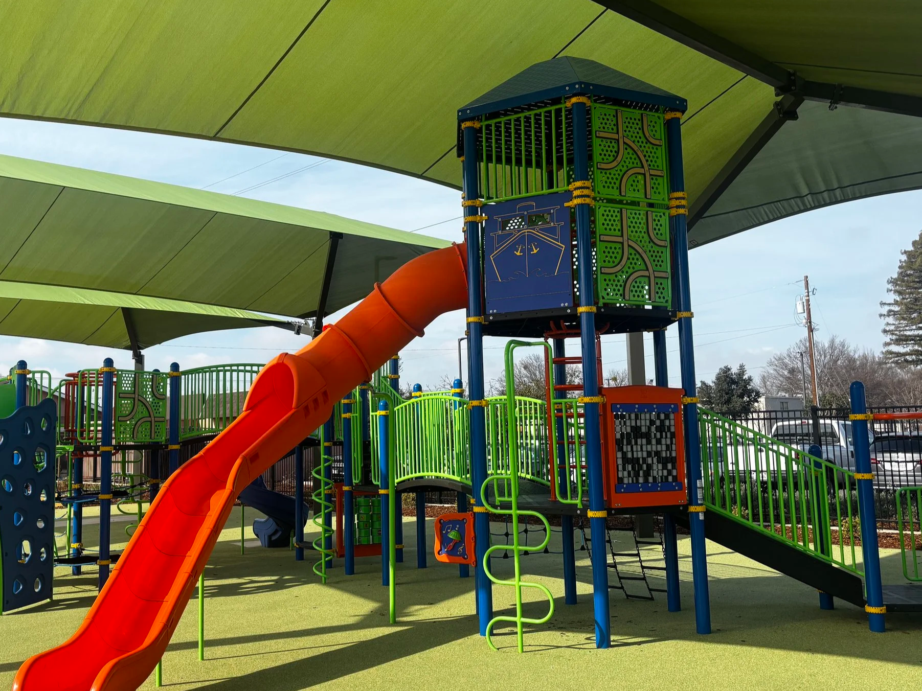 Colorful outdoor playground structure with slides, climbing areas, and shaded overhangs.