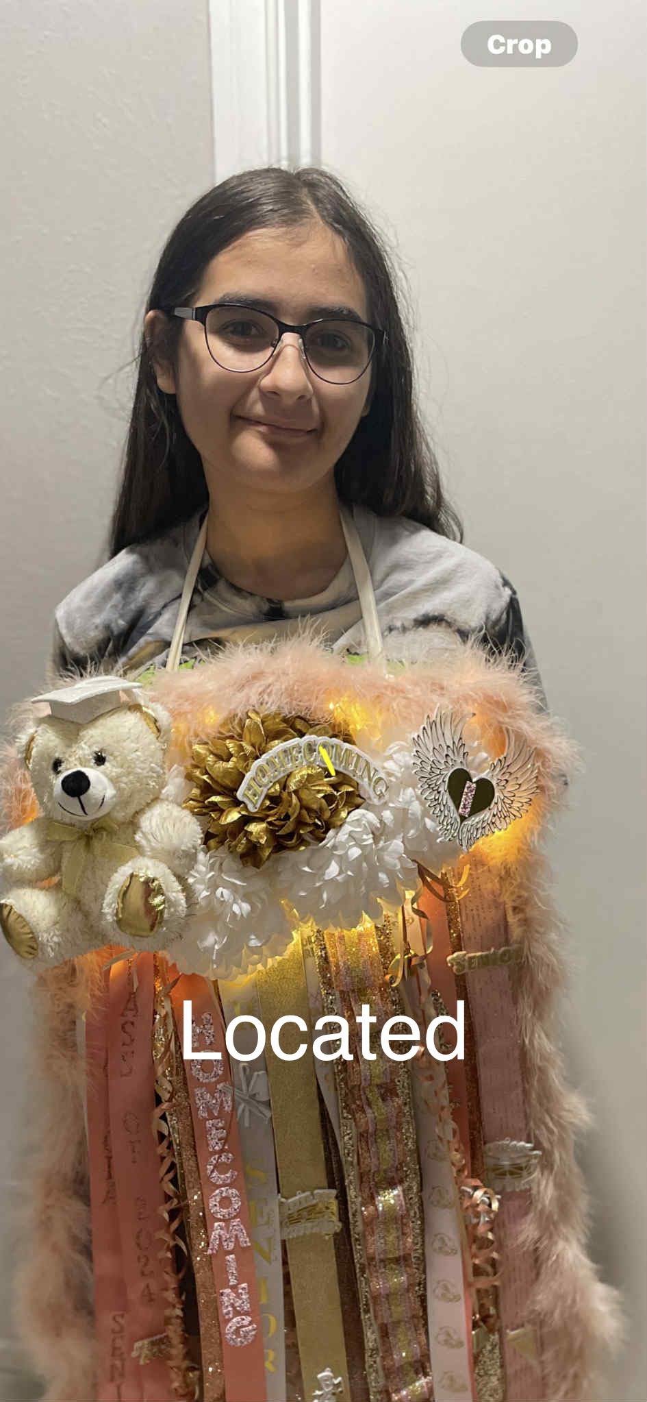 Young girl wearing glasses holding a decorative bouquet with ribbons, teddy bear, and heartfelt messages. The bouquet features a stuffed bear with a graduation cap, fluffy pink fabric, and lights.