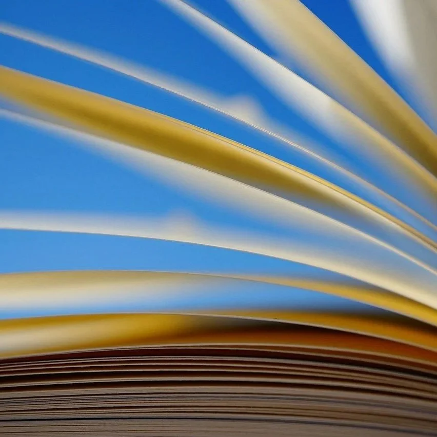 Close-up of colorful pages in an open journal or book with the sky visible through the pages.