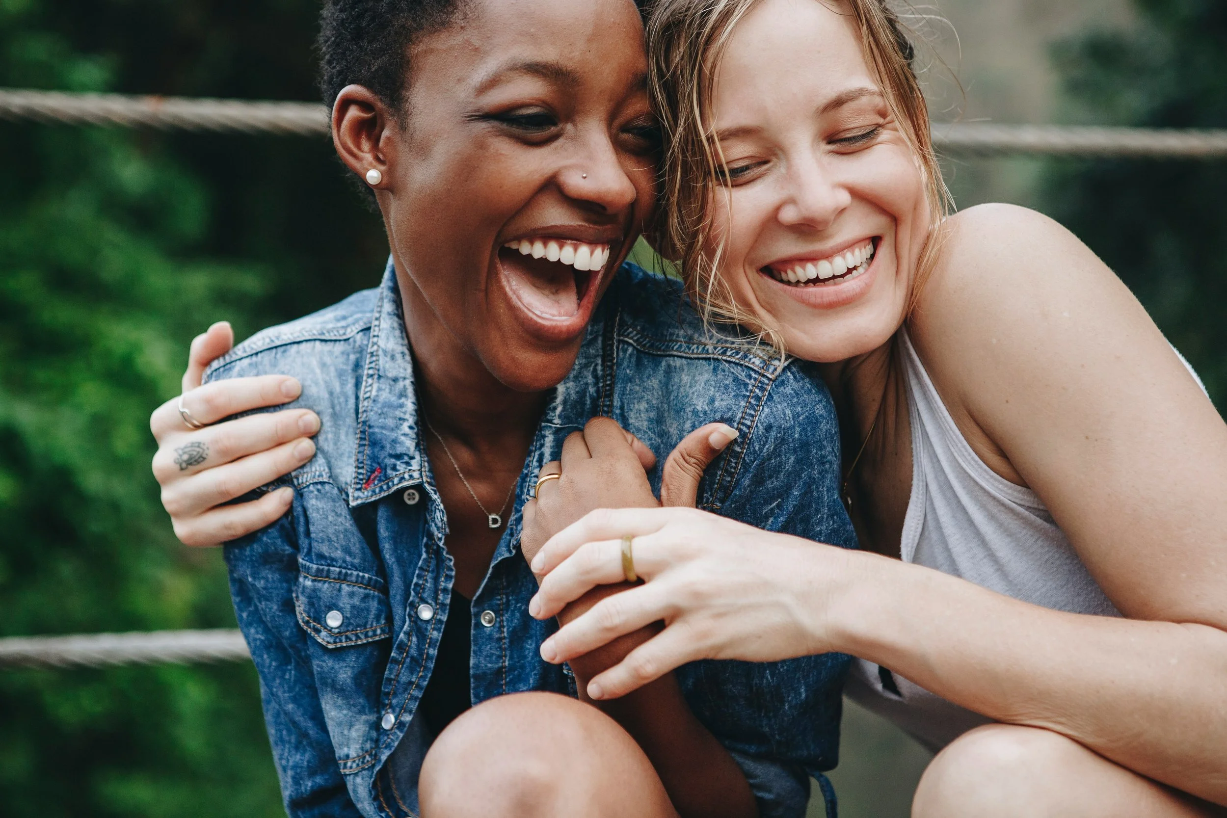 Two women laughing and embracing outdoors near a wooden fence