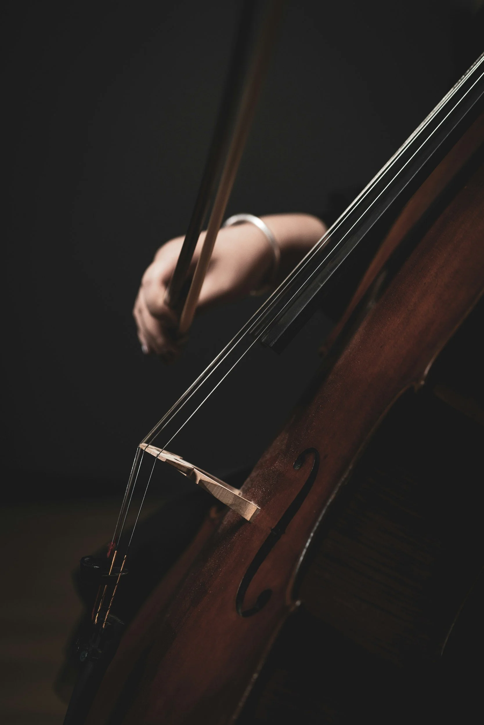 Close-up of a person playing a cello, focusing on their hand pressing the strings and the bow.