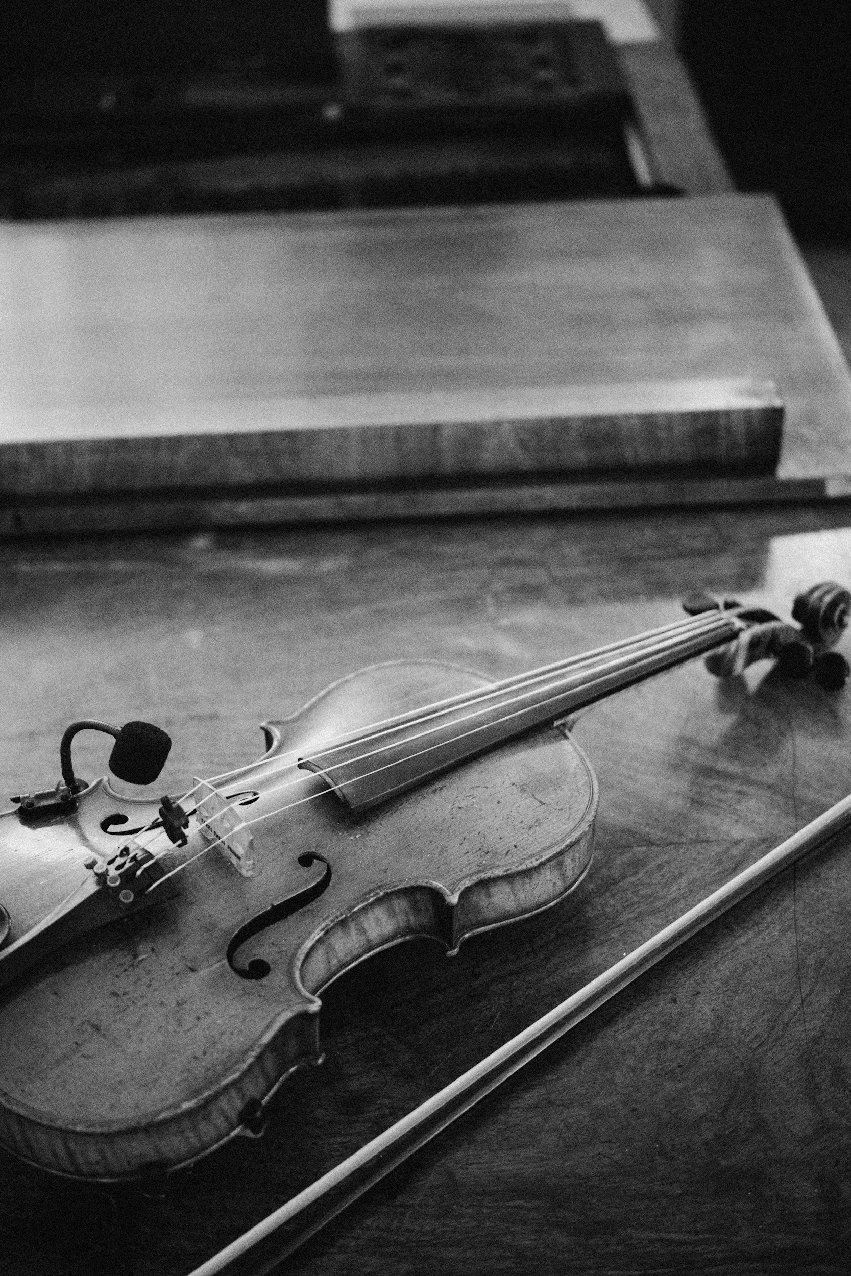 A violin rests on a wooden surface with its bow lying nearby. In the background, there are stacked vinyl records.