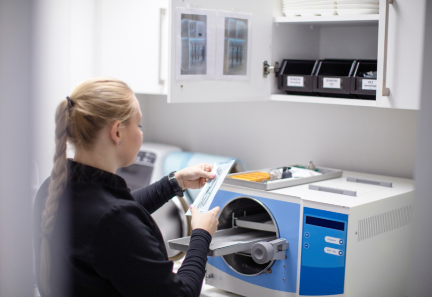 A woman in a medical lab reads a clipboard in a laboratory with equipment and storage bins around.