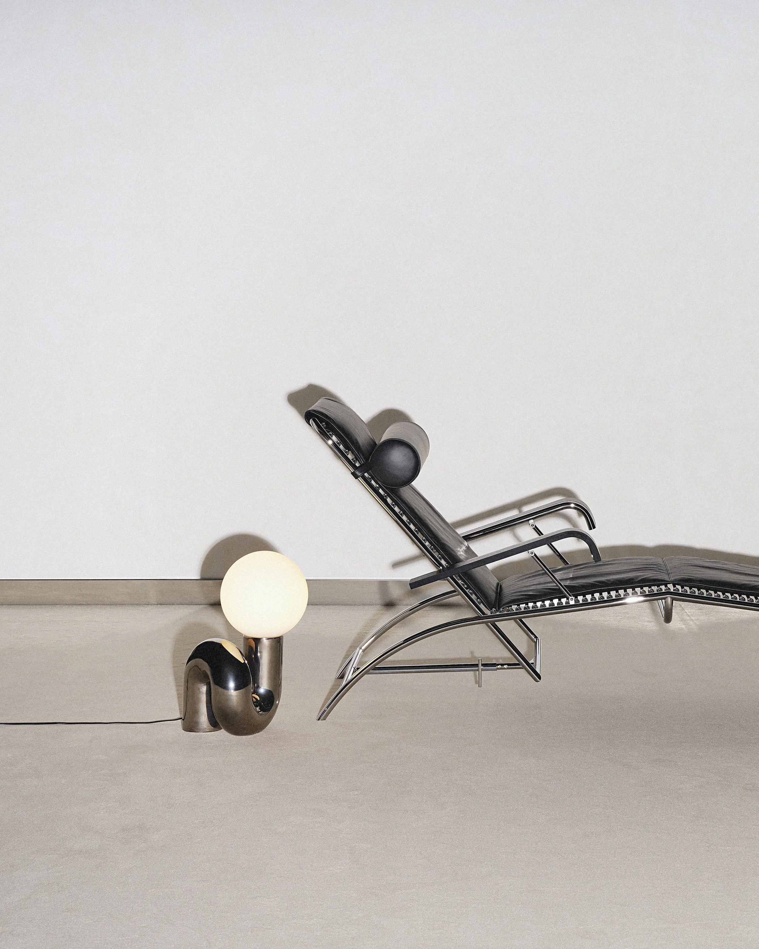 Fauteuil noir en métal et un luminaire en forme de tube avec une ampoule blanche dans un espace minimaliste.