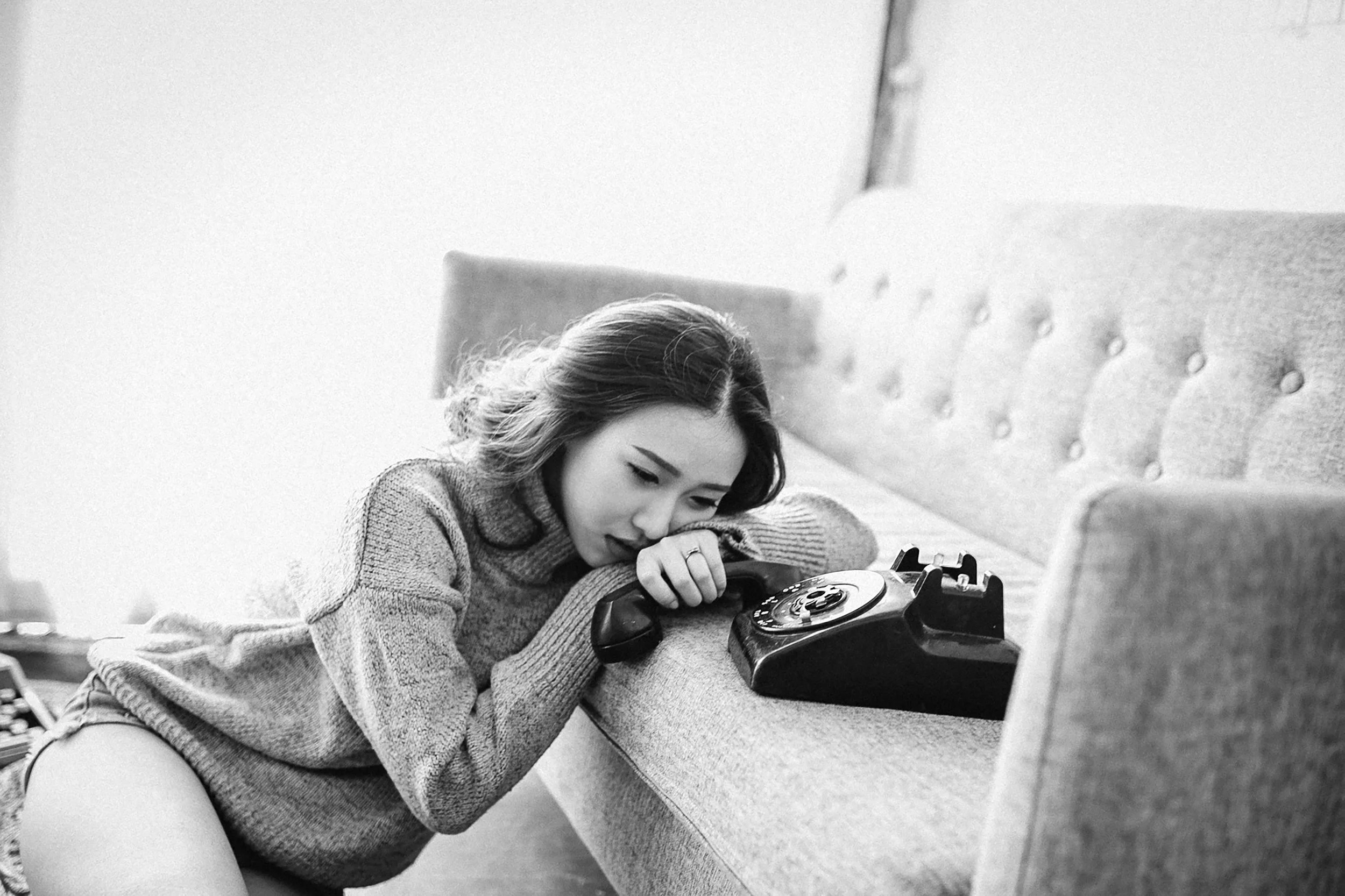 A woman with long hair leaning on a table while talking on a rotary dial telephone.