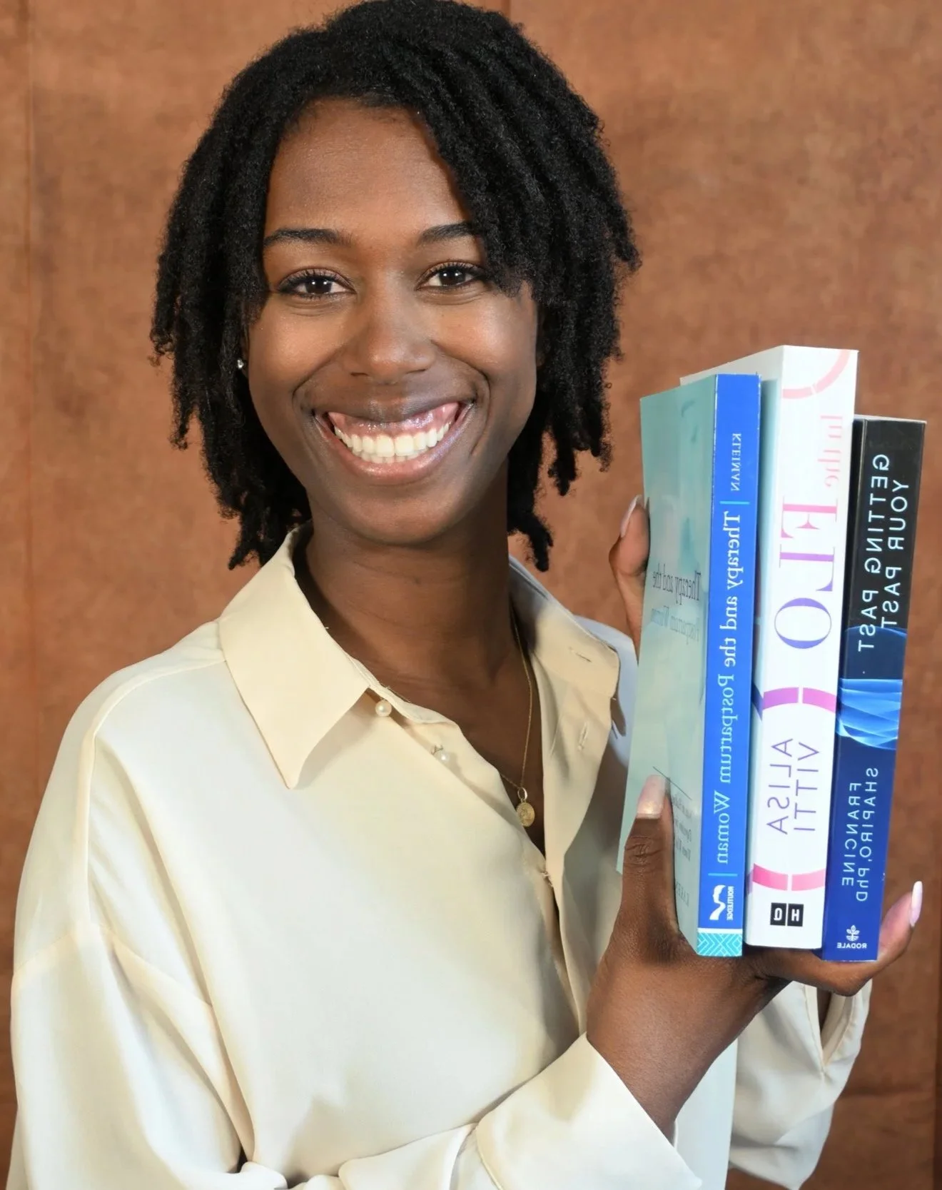 A woman with short curly hair smiling and holding a stack of books.