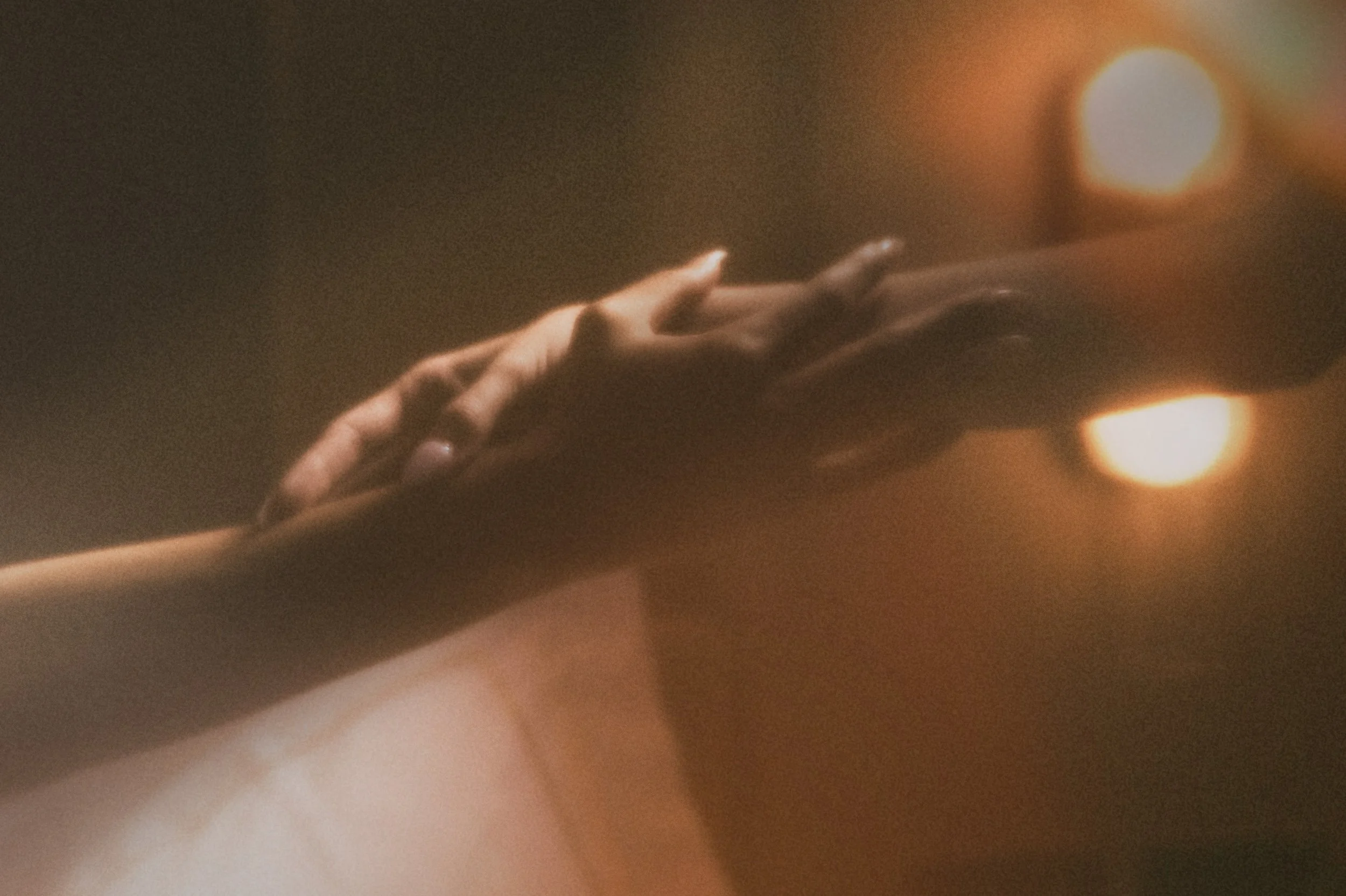 A hand reaching toward the warm glow of two burning candles.