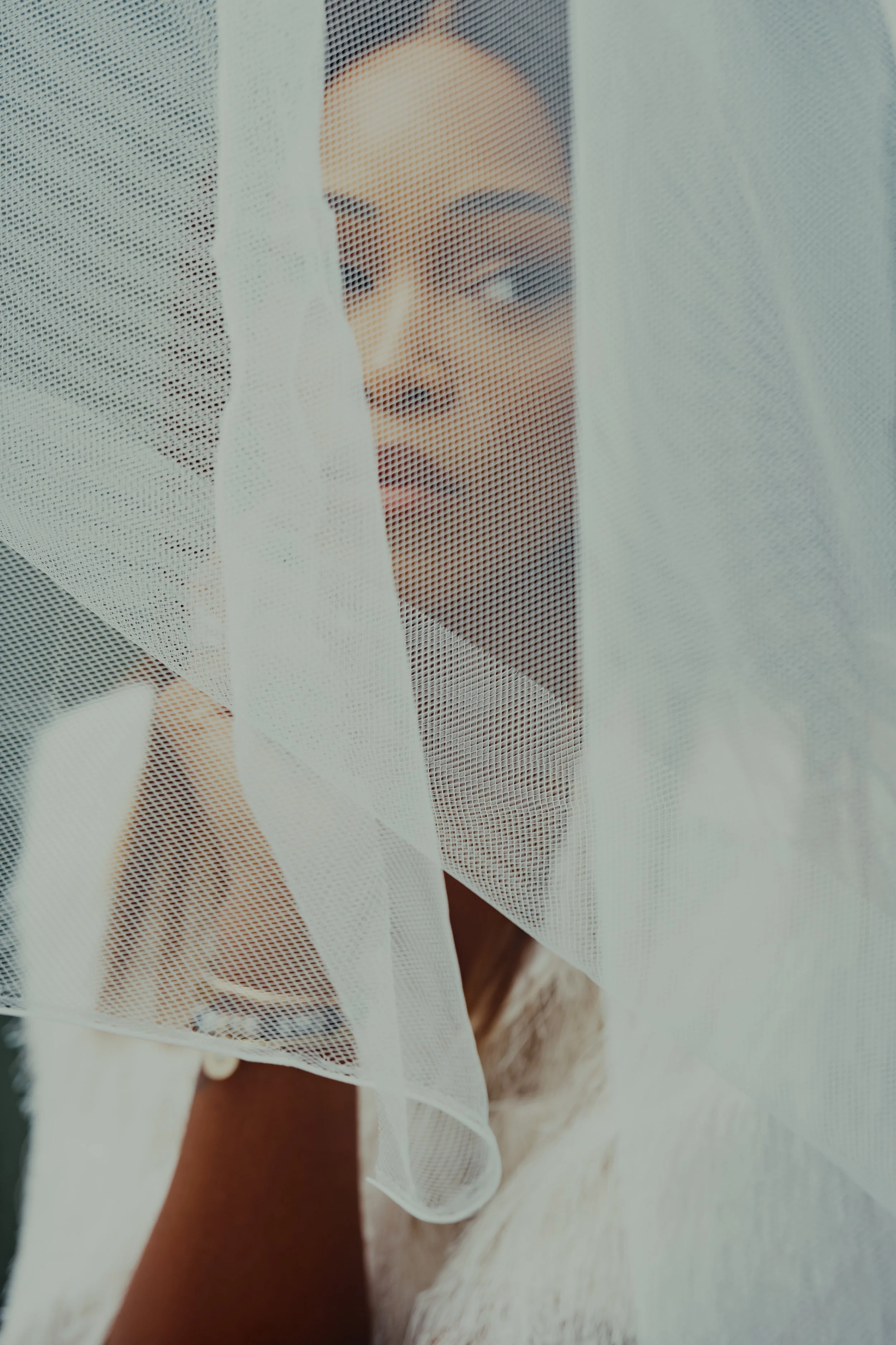 A woman peering through a sheer, white curtain, with her face partially obscured and lips slightly parted.