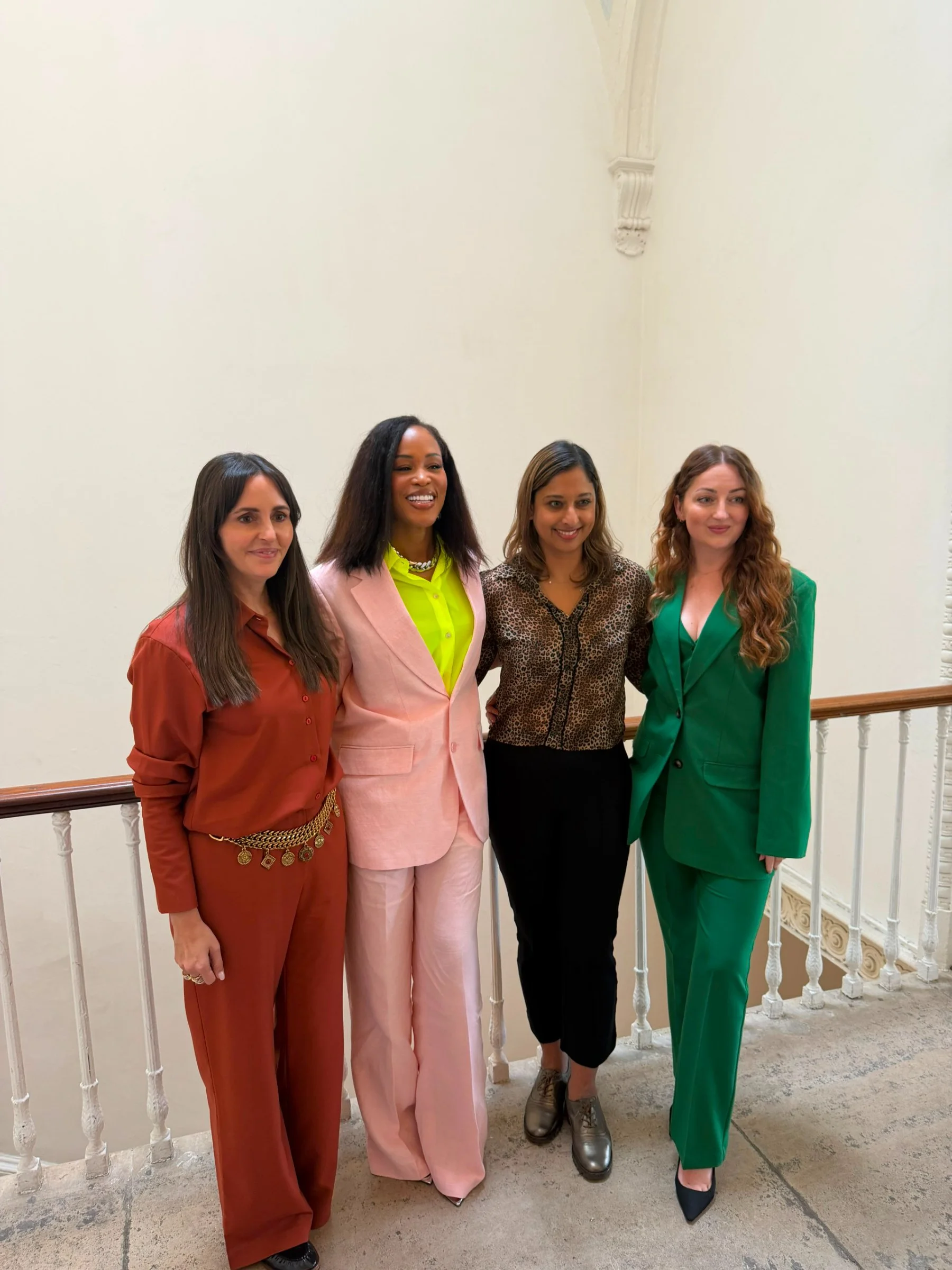 Four women wearing colorful suits standing together indoors, smiling for a group photo.