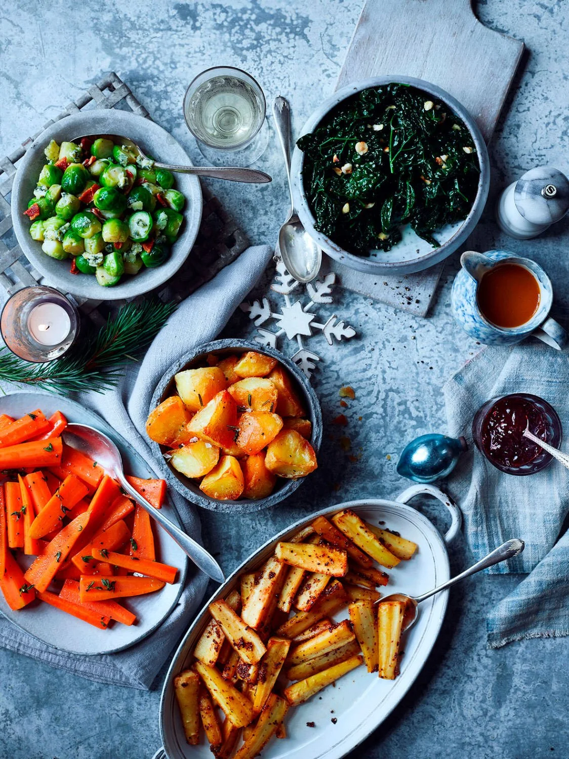 Winter holiday feast with roasted vegetables, leafy greens, and beverages on a table.