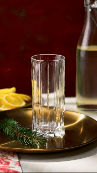 A clear empty glass placed on a gold-colored tray with a sprig of pine and lemon slices, background features a glass bottle of water with a lemon slice.
