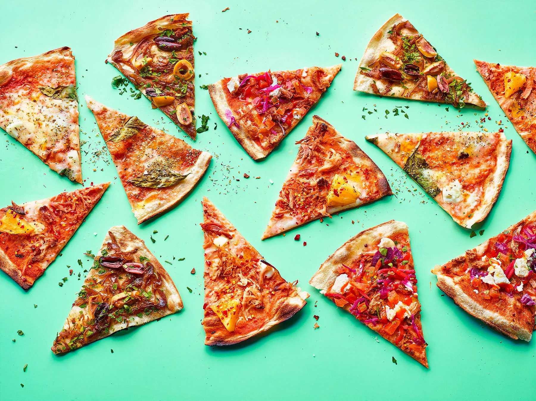 Multiple slices of pizza with various toppings scattered on a light green surface.