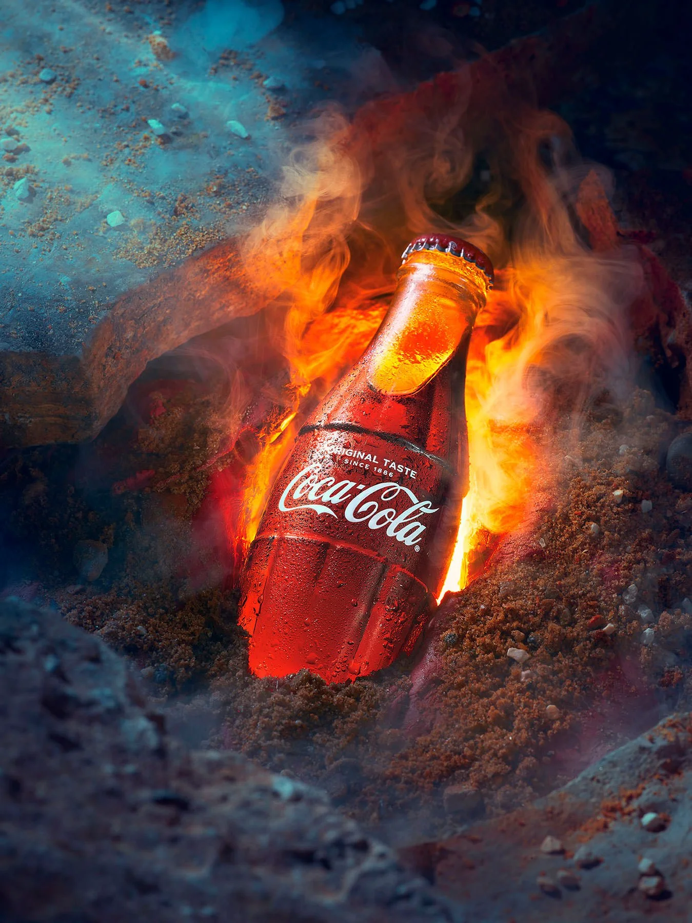 Ryan Ball food photographer — A Coca-Cola glass bottle on fire in a smoky, rocky setting,  commercial food photography London