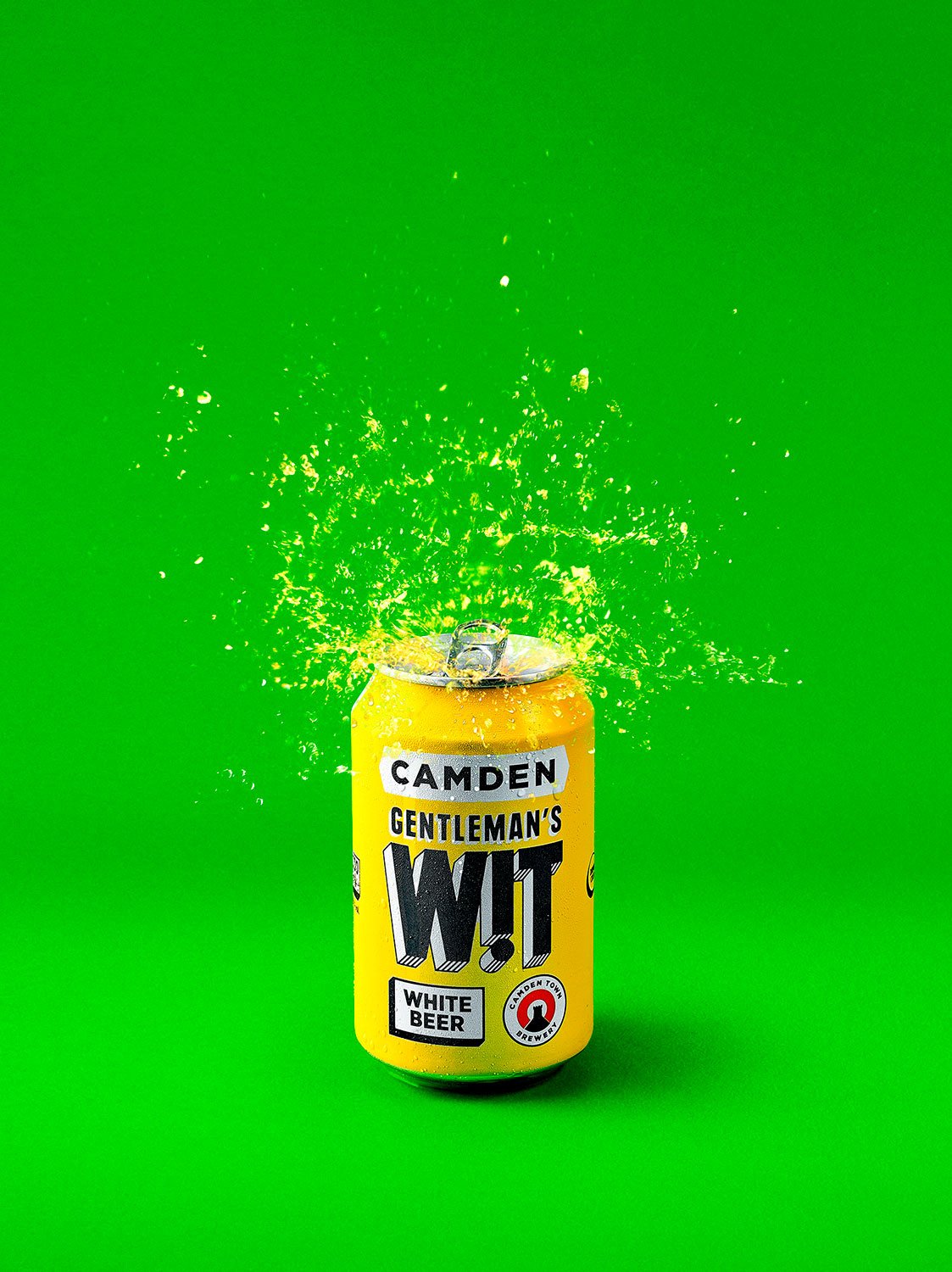 A yellow can of Camden Gentleman's W!T White Beer exploding, with liquid and foam splashing upwards, against a bright green background.
